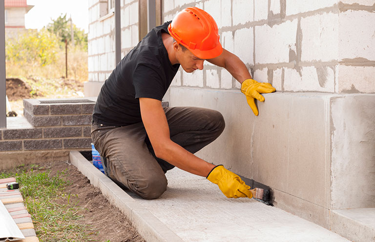 man sealing exterior of house foundation