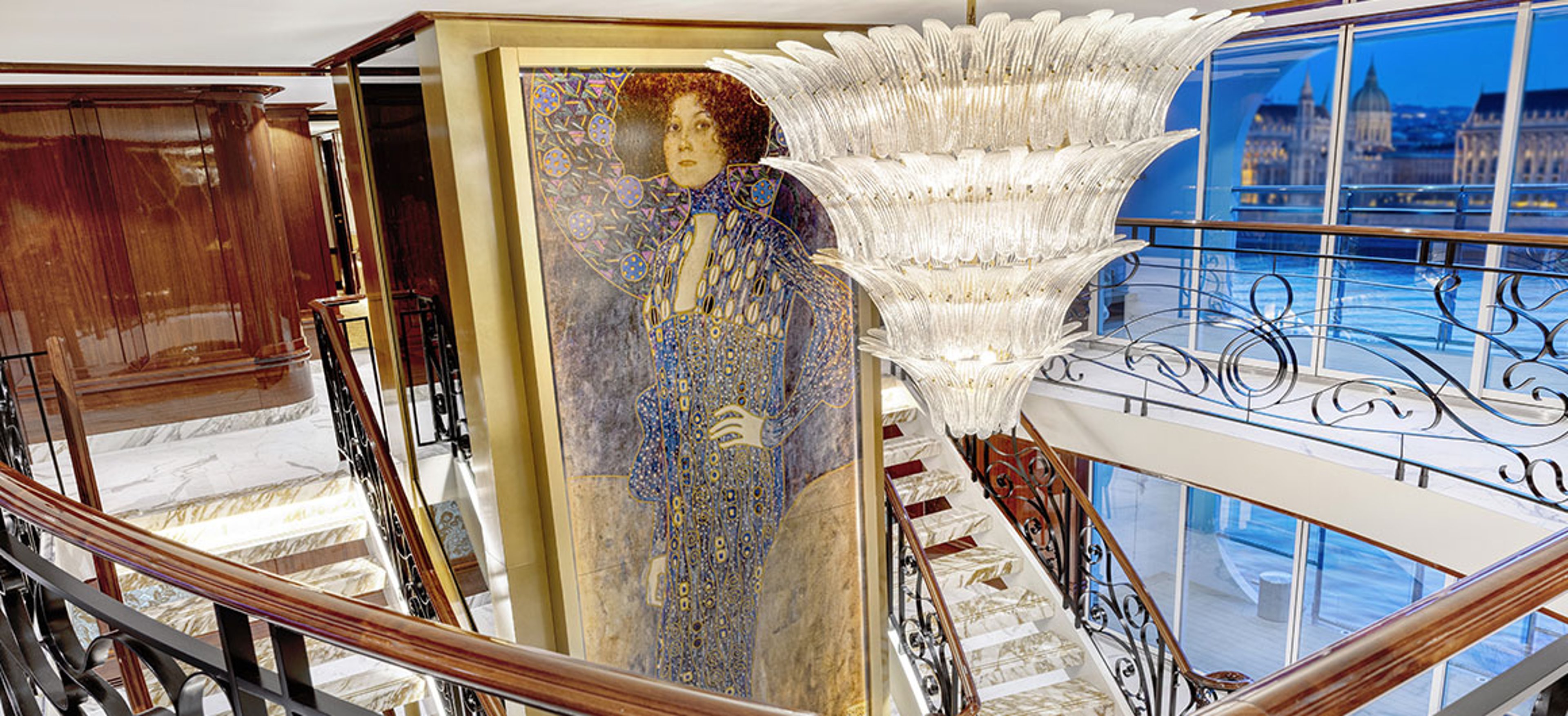 Illuminated marble staircase with ornate black railings and a large portrait at the center aboard the S.S. Emilie.