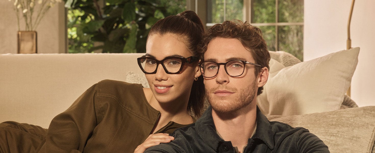 Man and woman sitting on couch, both wearing glasses