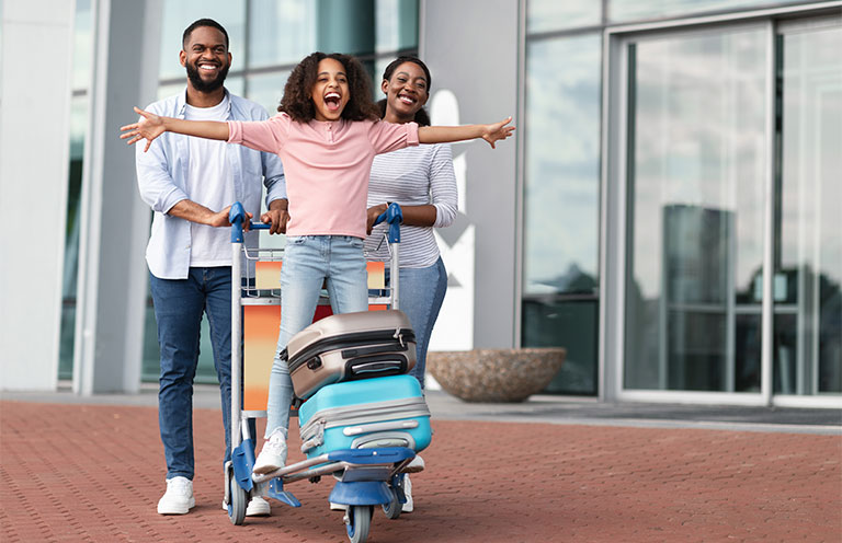 mom and dad pushing daughter on suitcase dolly