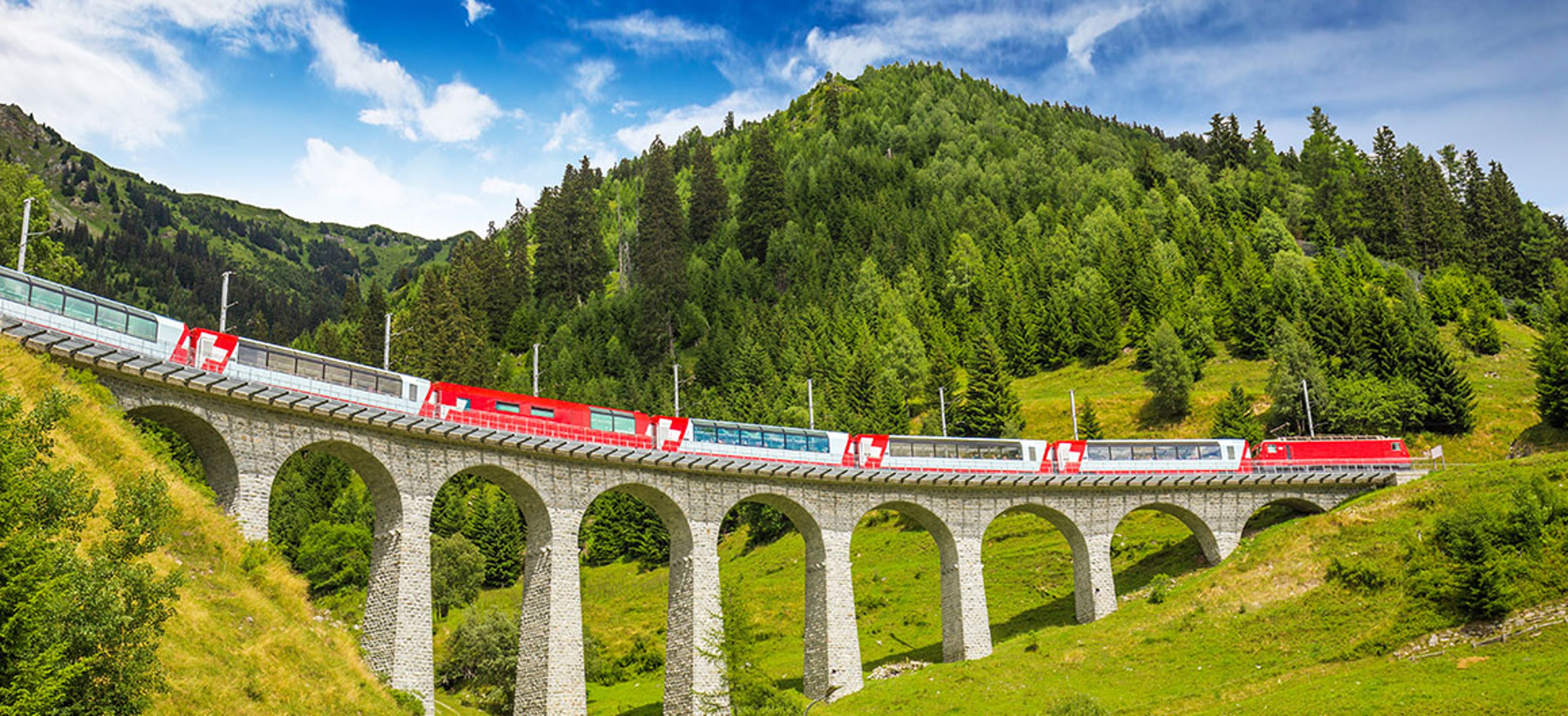 Train crossing a tall stone viaduct surrounded by green mountain scenery.