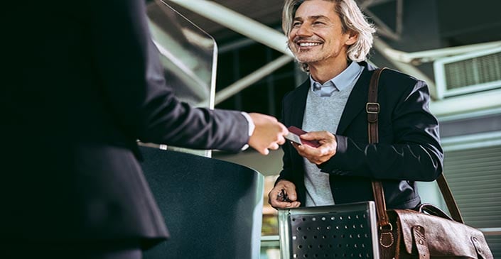 A smiling man at an airport check-in counter handing over a passport.