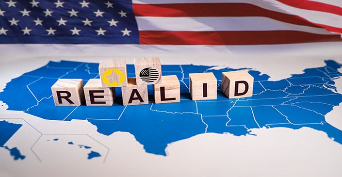Wooden blocks spelling "REAL ID" on a map of the USA with an American flag in the background.