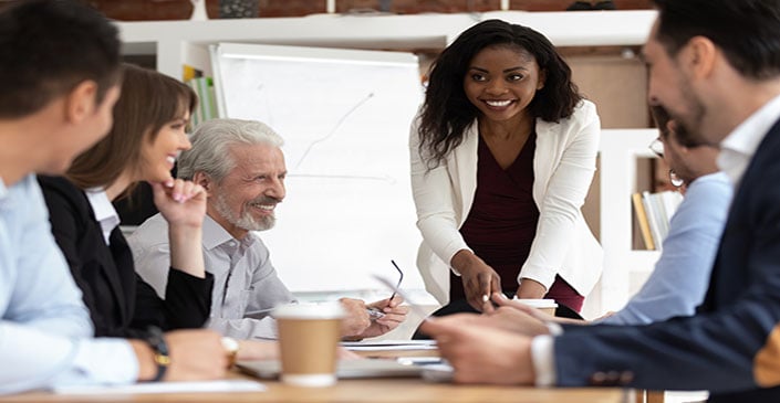People in a business meeting, with a woman in a white blazer leading the discussion.