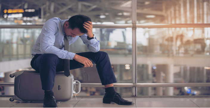 Man sitting on a suitcase in an airport, looking distressed.
