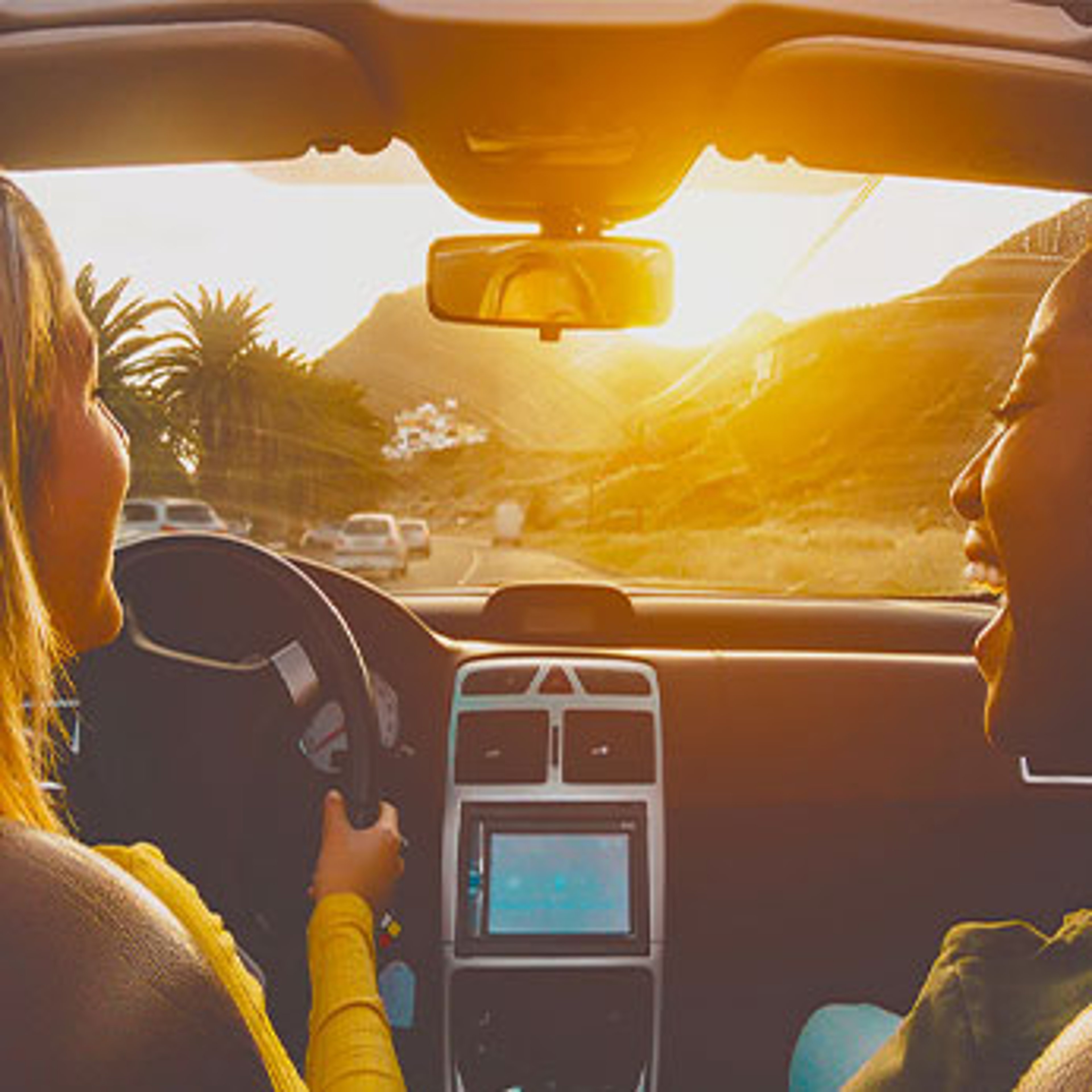 Two women inside car driving on road with palm trees