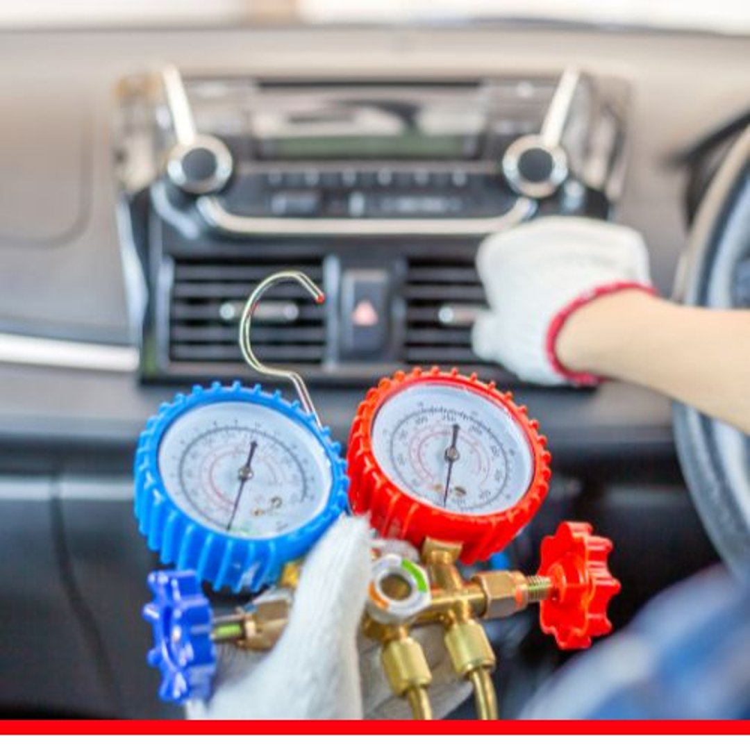 A pair of car A/C manifold pressure gauges with blue and red encasements inside a vehicle.