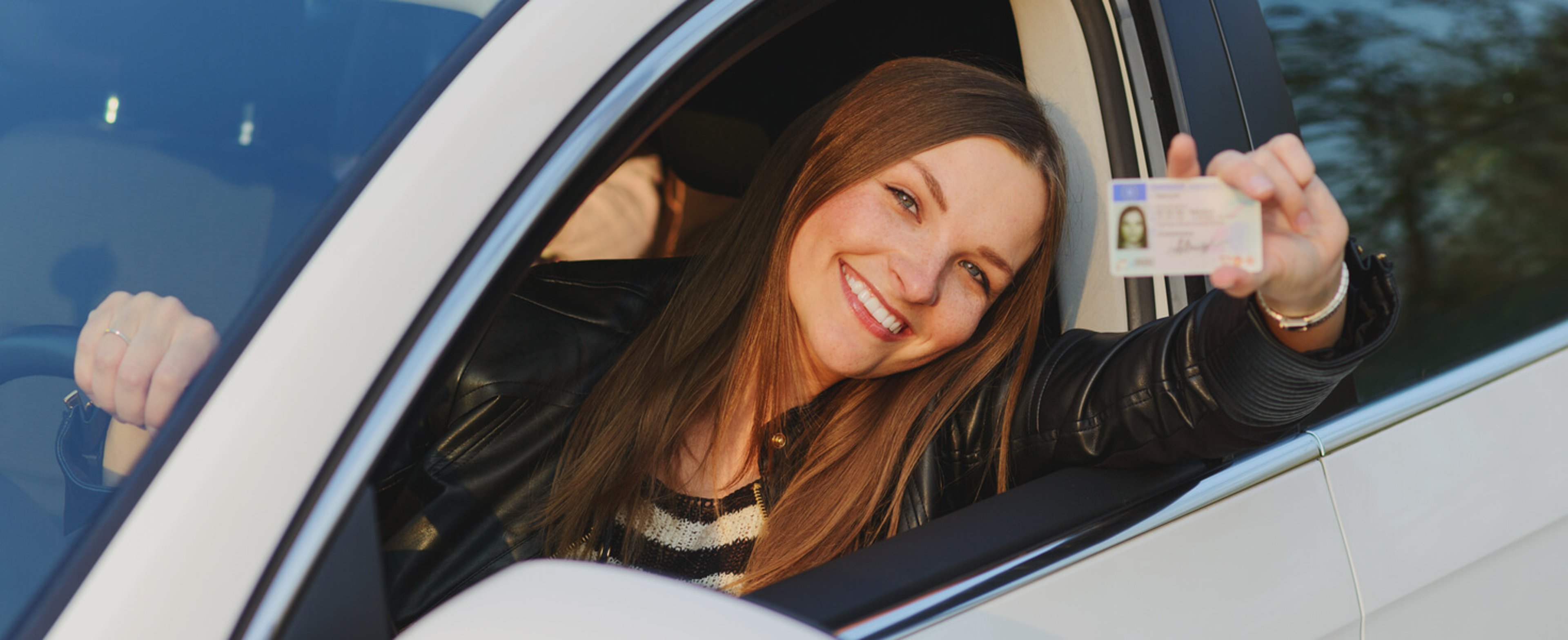 Young driver smiling in the driver's seat and holding up her license