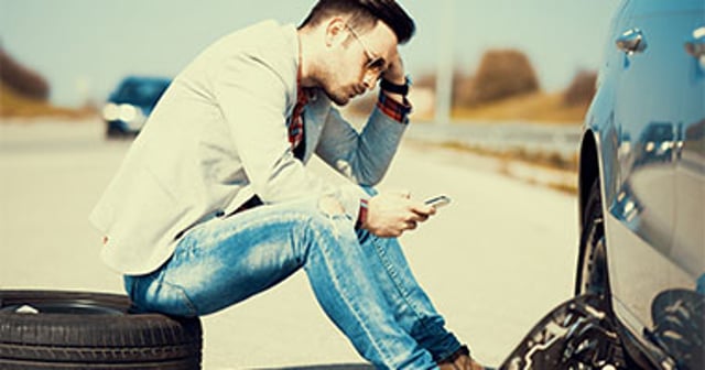 Man sitting on curb calling for roadside service