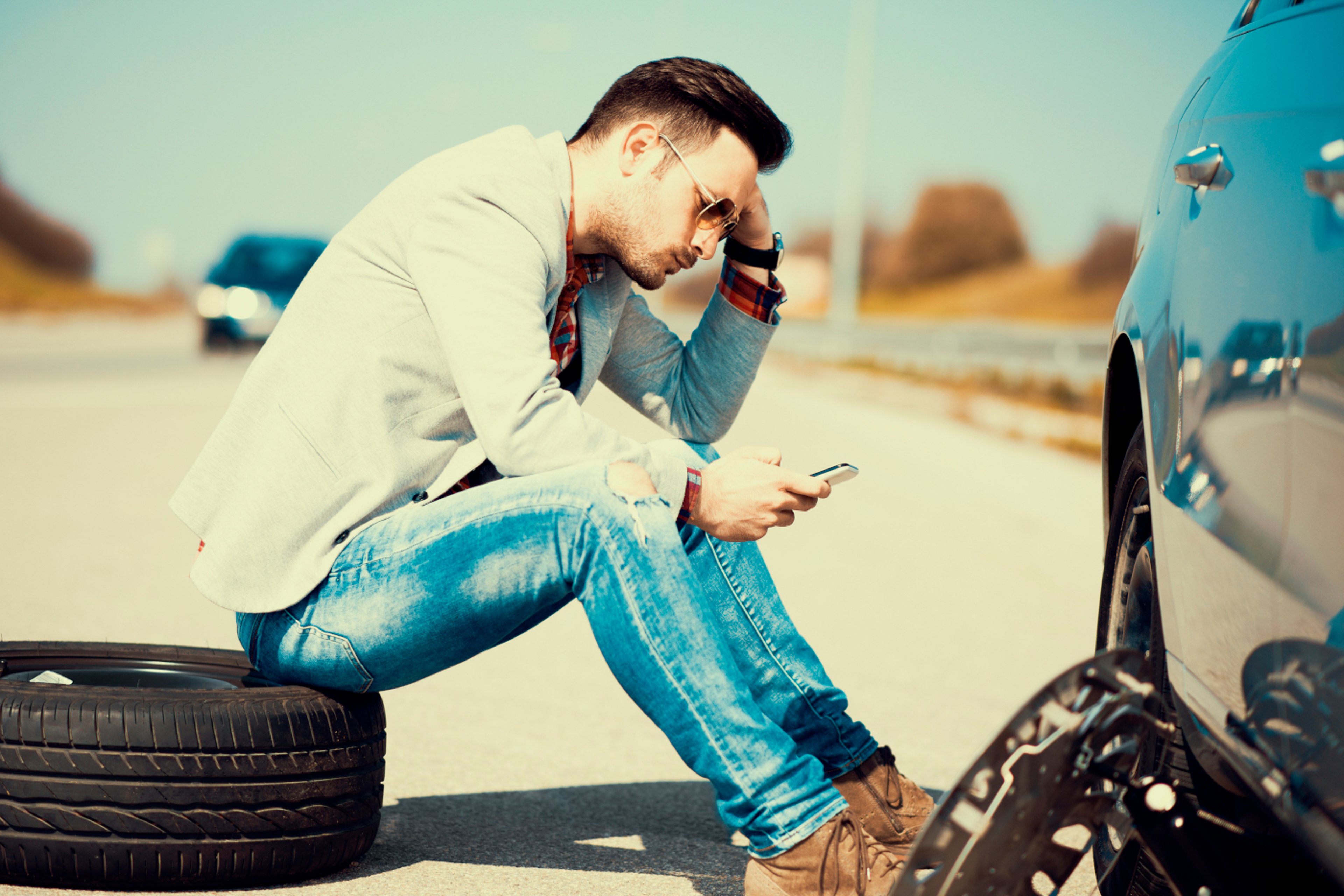 Man sitting on curb calling for roadside service