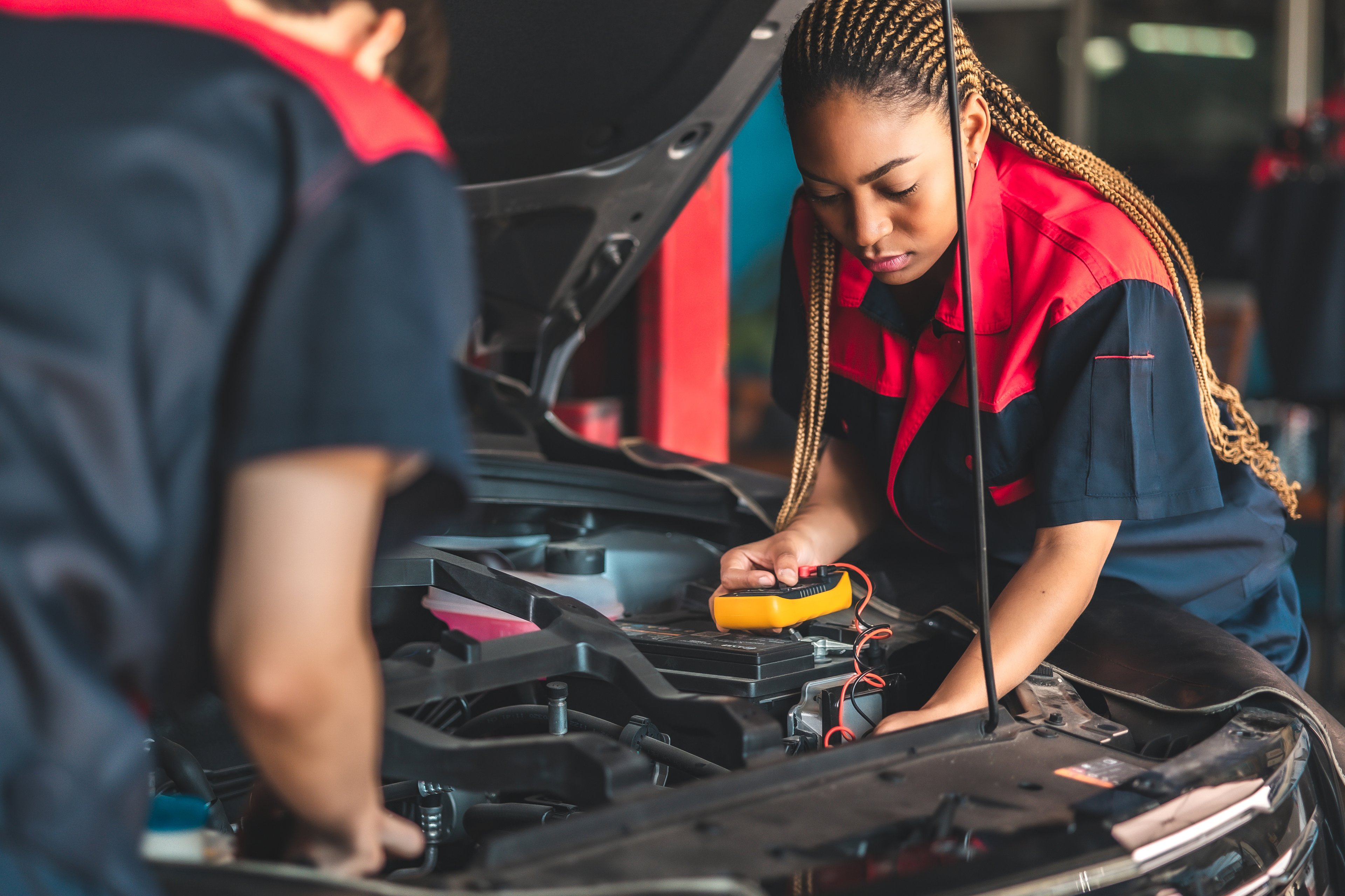 Two mechanics (One woman and one man) inspect the battery health of a car in a repair shop 