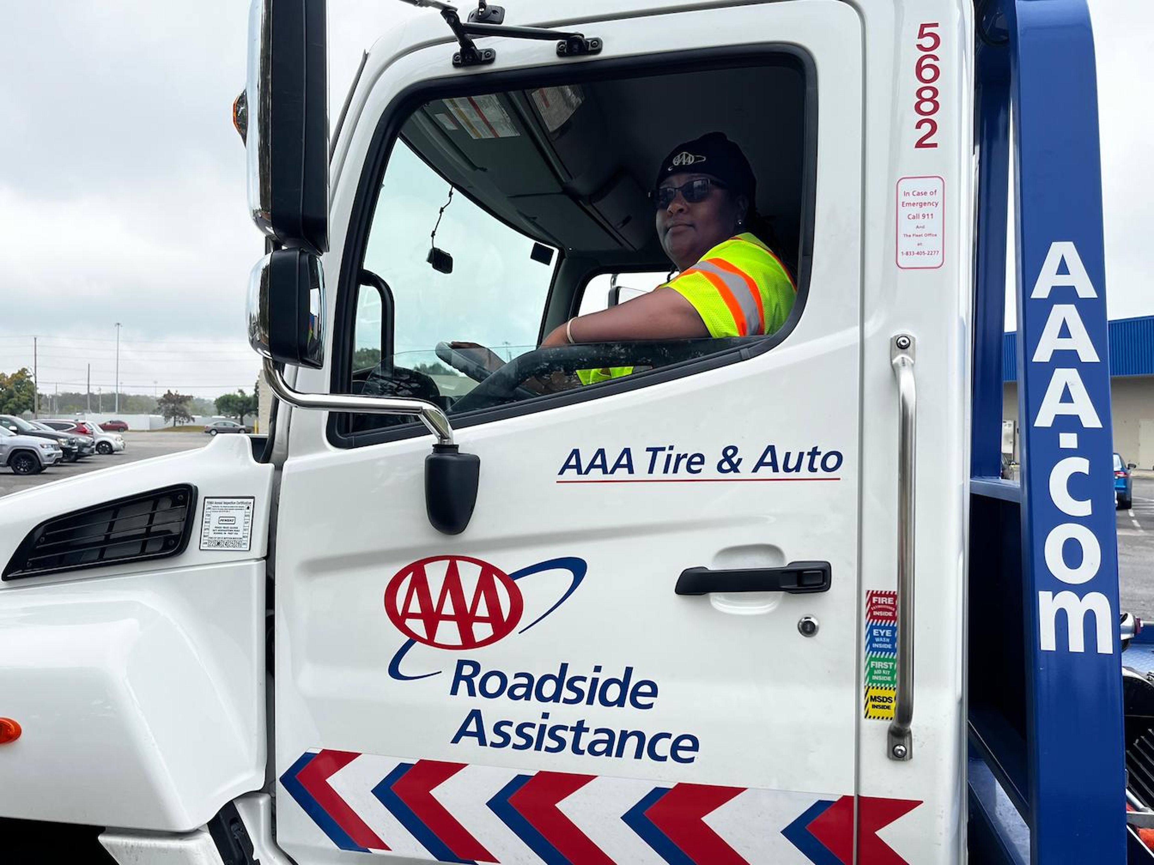 A person in a high-visibility vest and sunglasses sits in the driver's seat of an AAA Roadside Assistance truck.