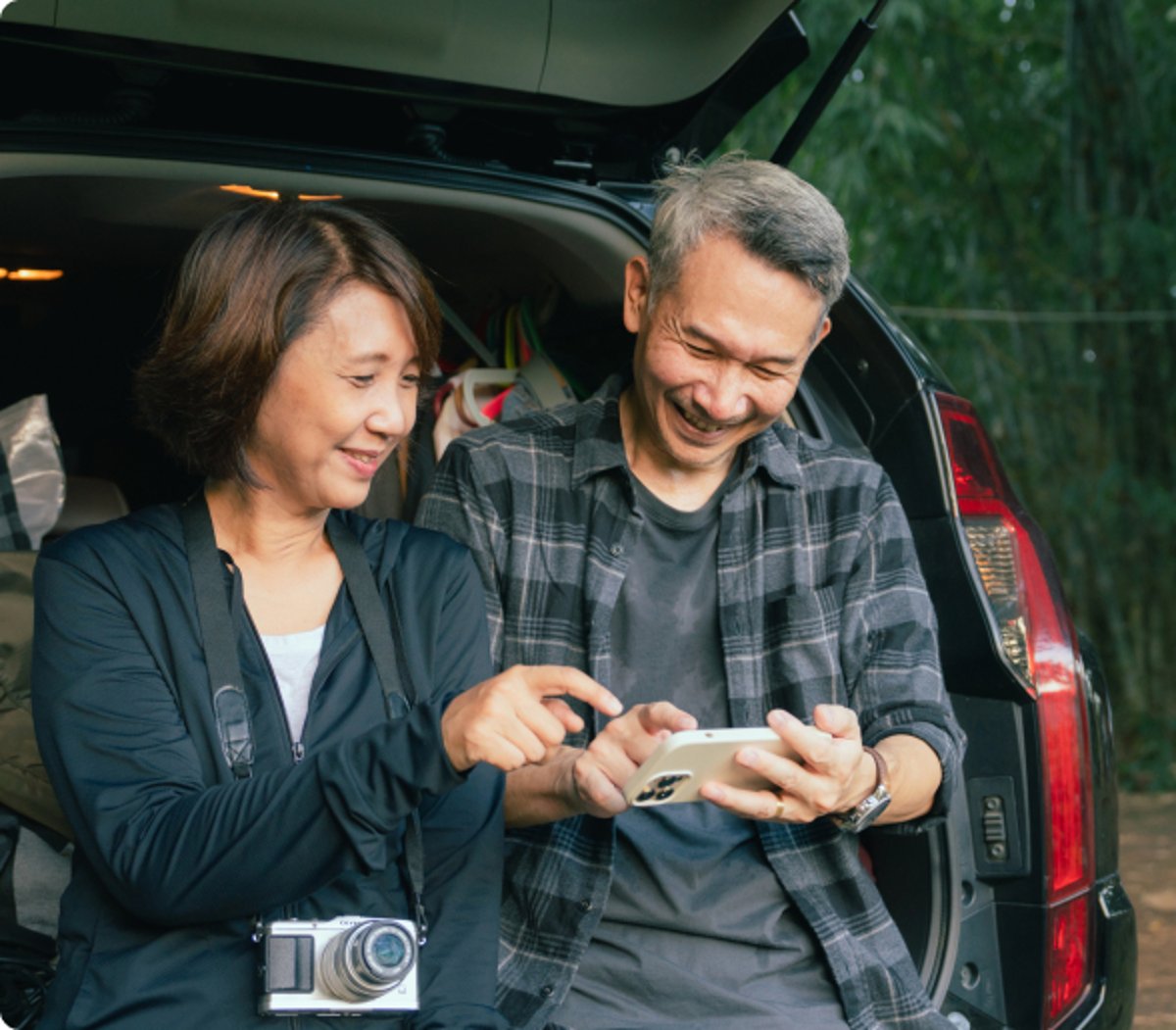 Two very happy AAA members standing by their car and looking at a smartphone