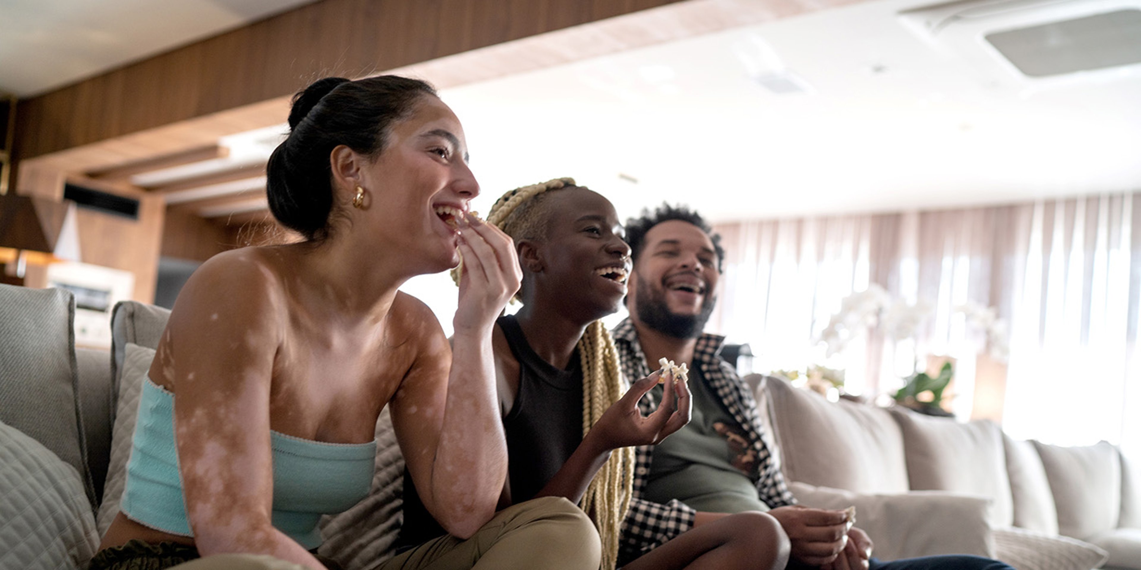 Three friends watching a movie on the couch, enjoying popcorn.