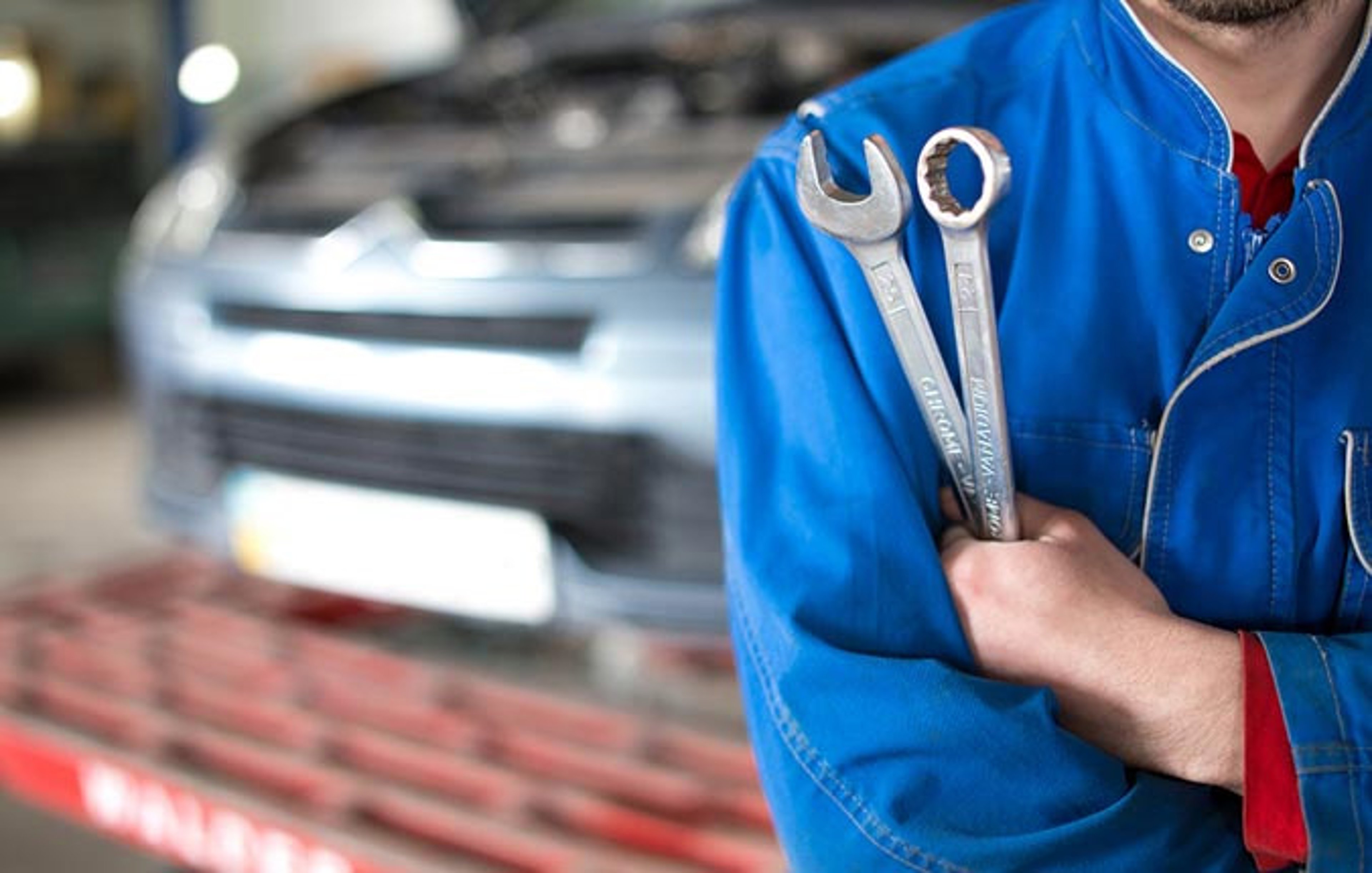 Mechanic holding wrenches in front of car