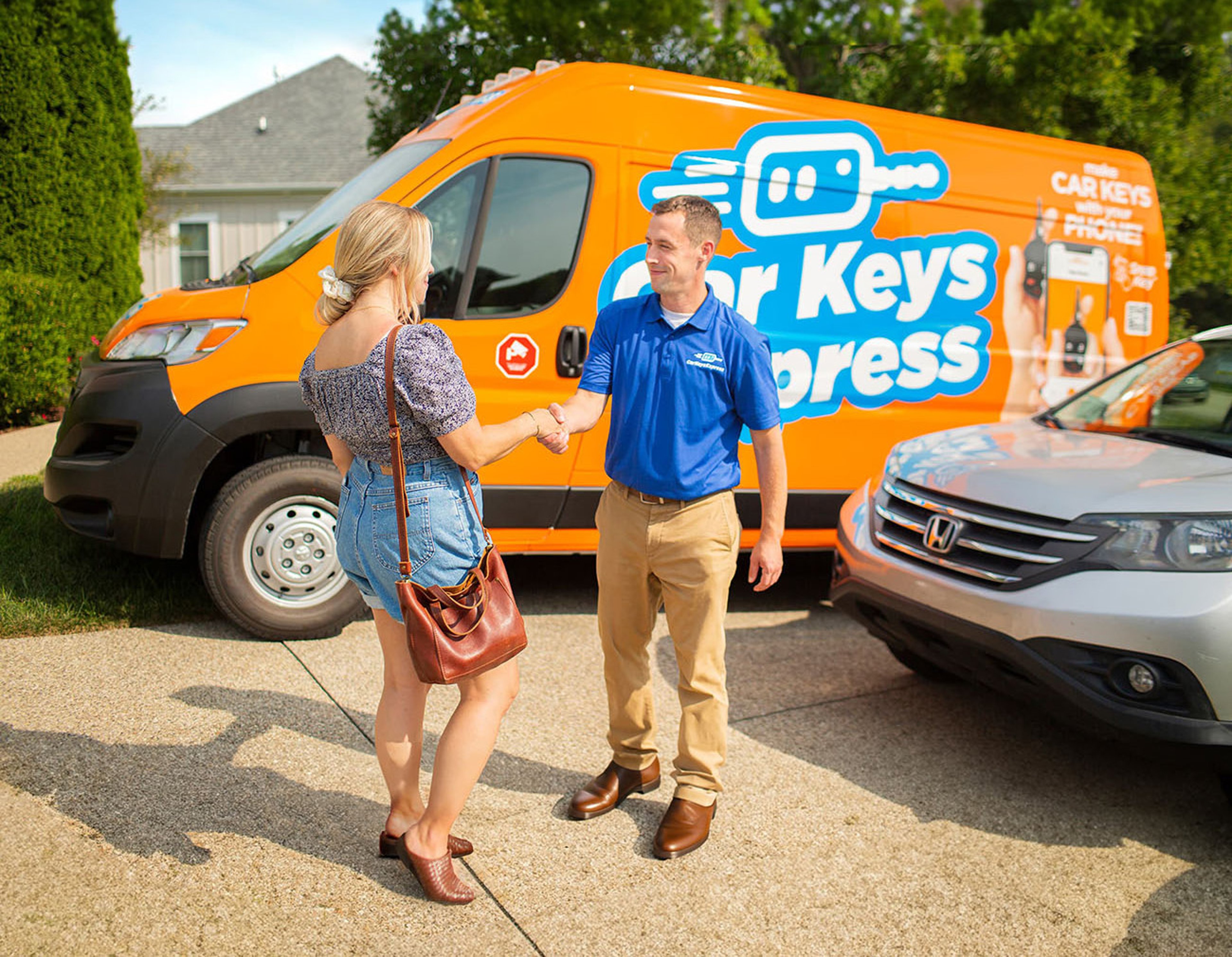Car Keys Express technician in blue shirt shaking hands with customer outside her home after lockout