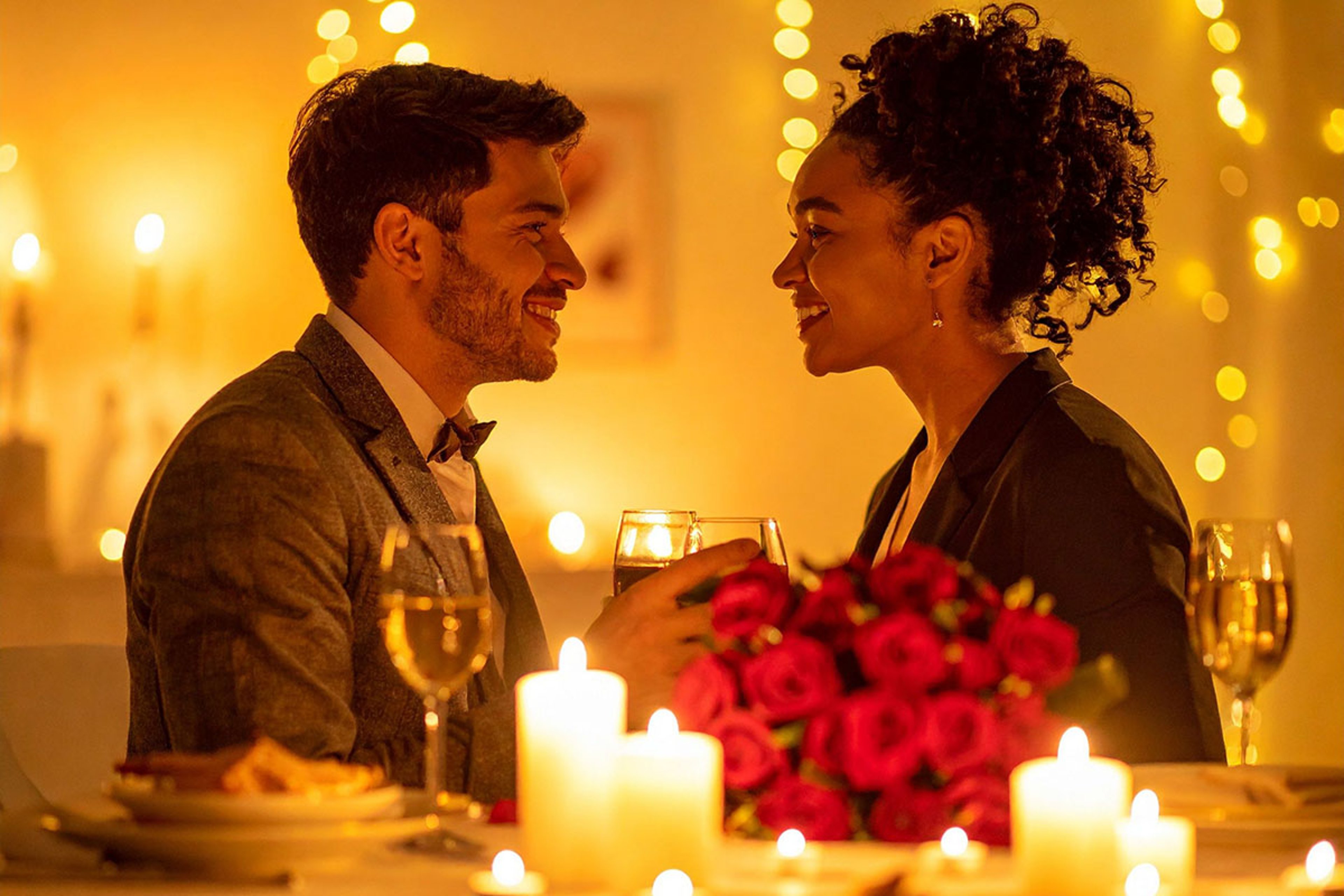 A man and a woman smiling at each other across a table during a romantic candlelight dinner.