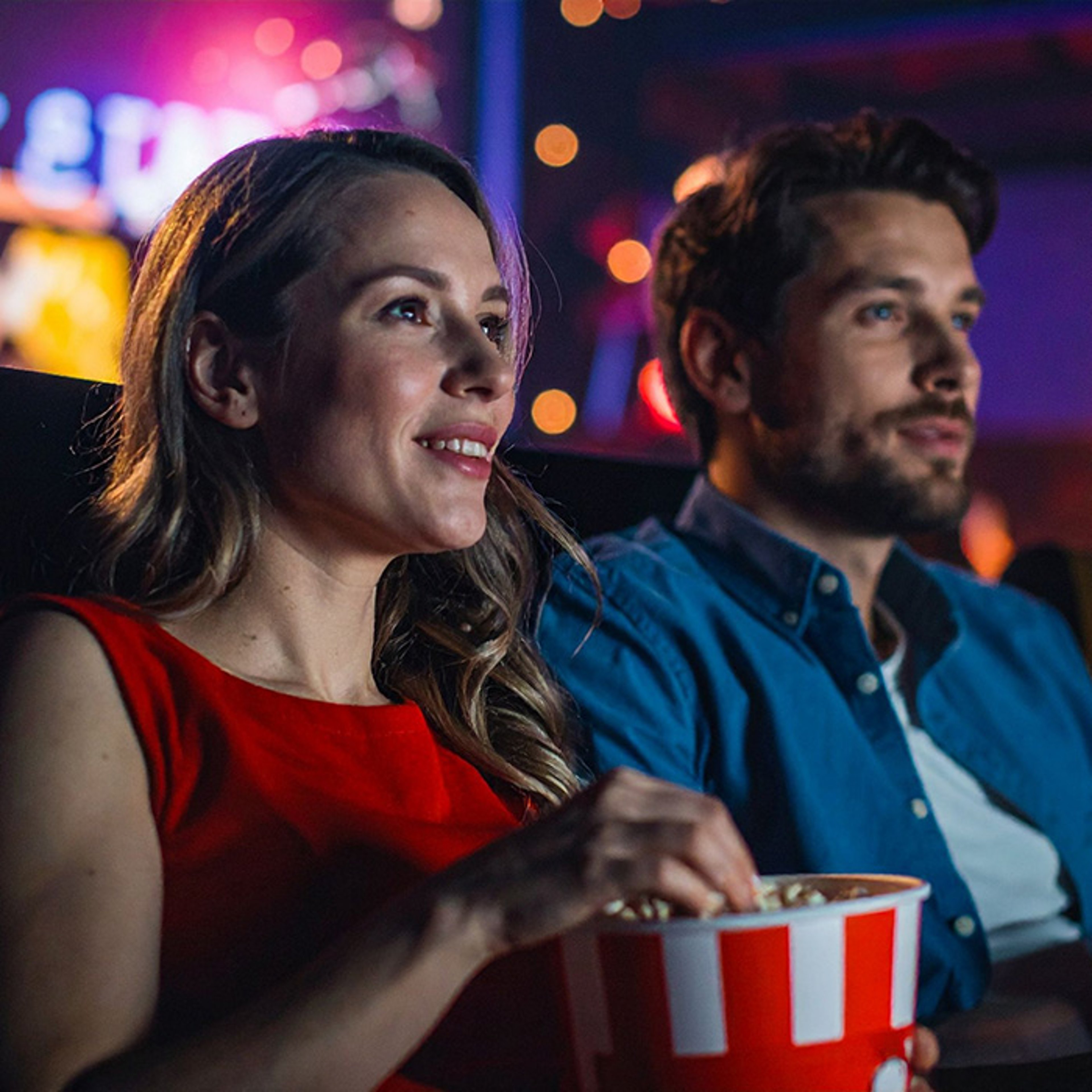 A man and a woman watching a movie in a theater while eating popcorn.