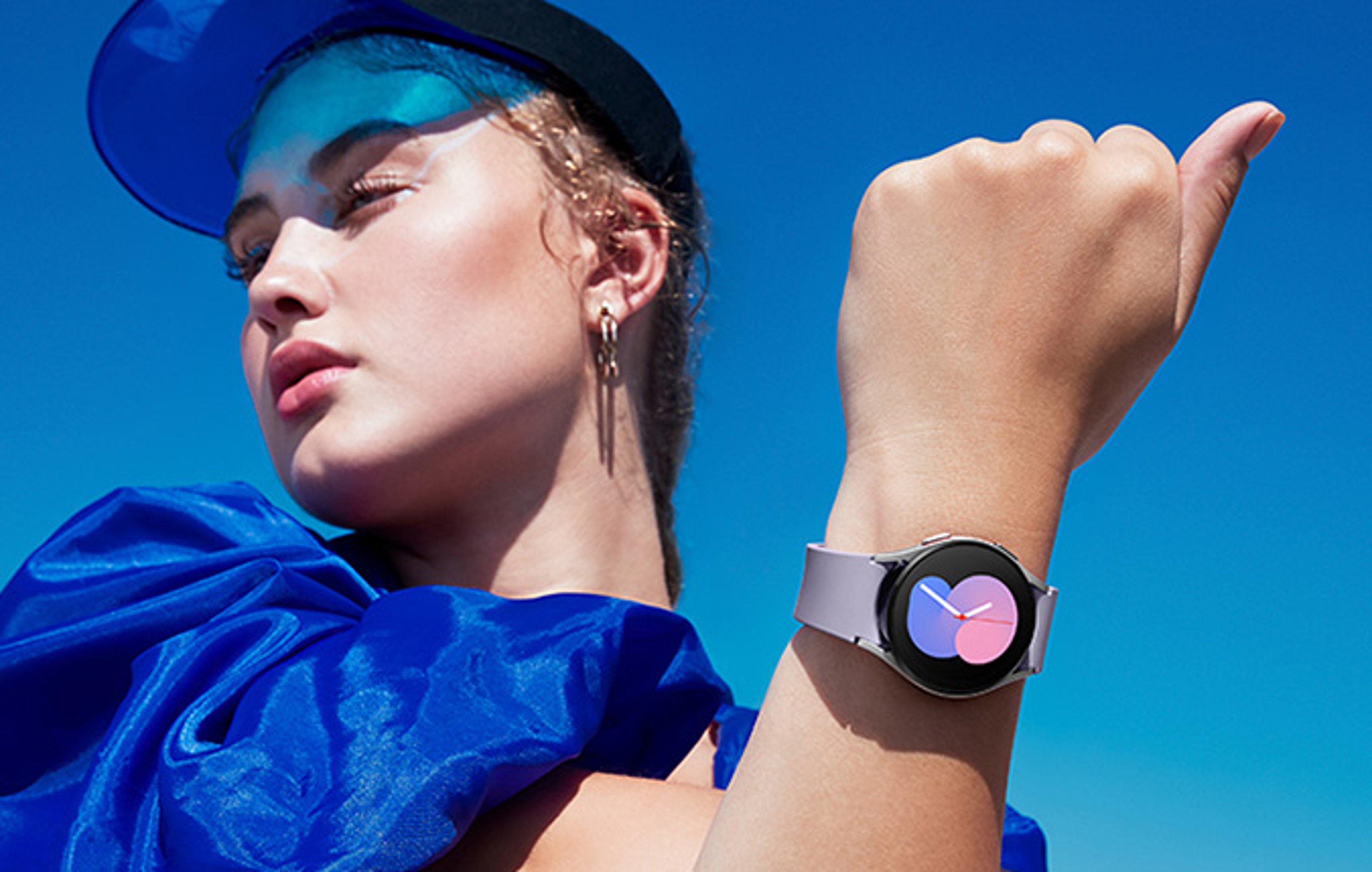 Woman wearing designer blue outfit and cap, showing smartwatch on wrist.