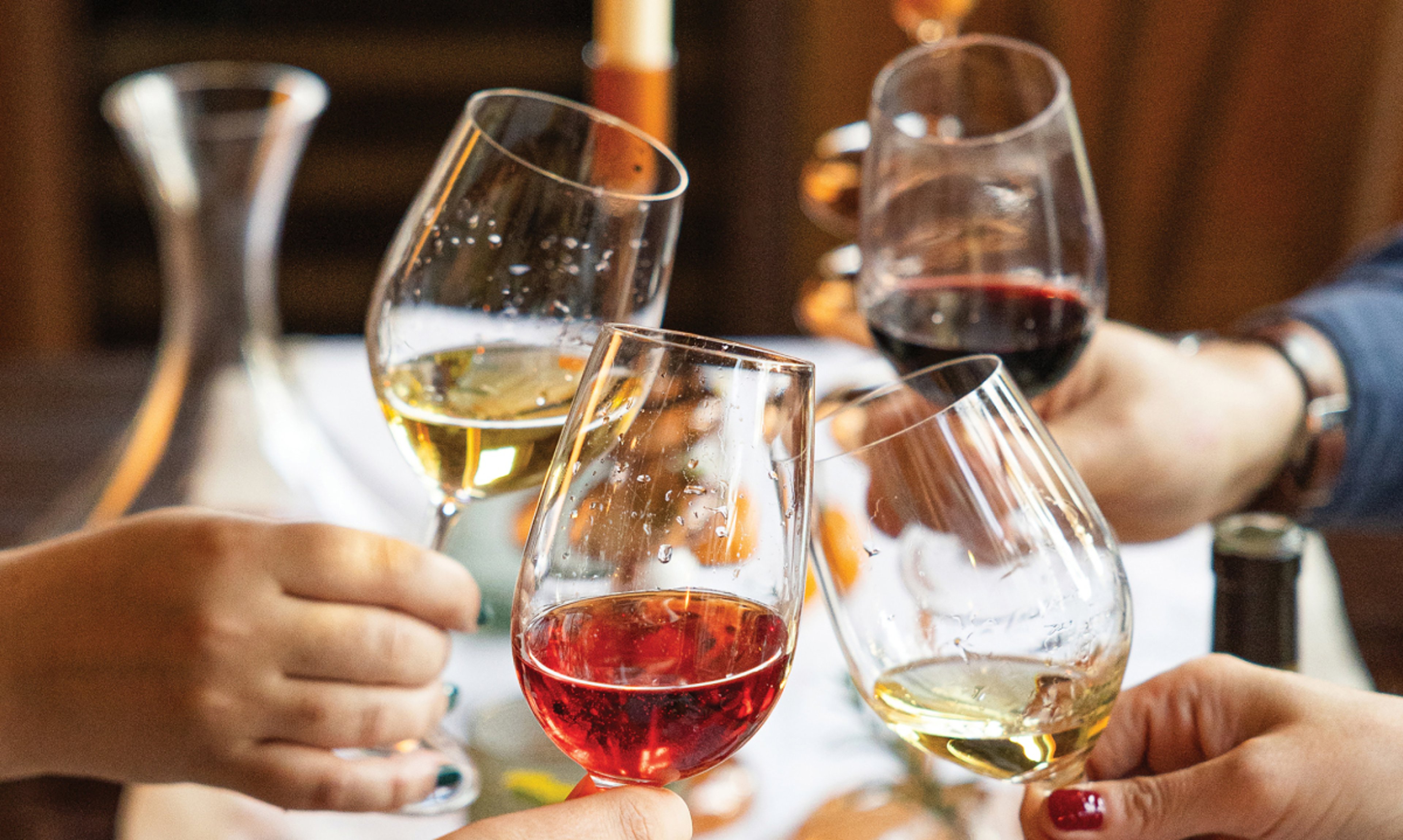 Close up of group of people toasting at dinner table with four different hued wines in glasses