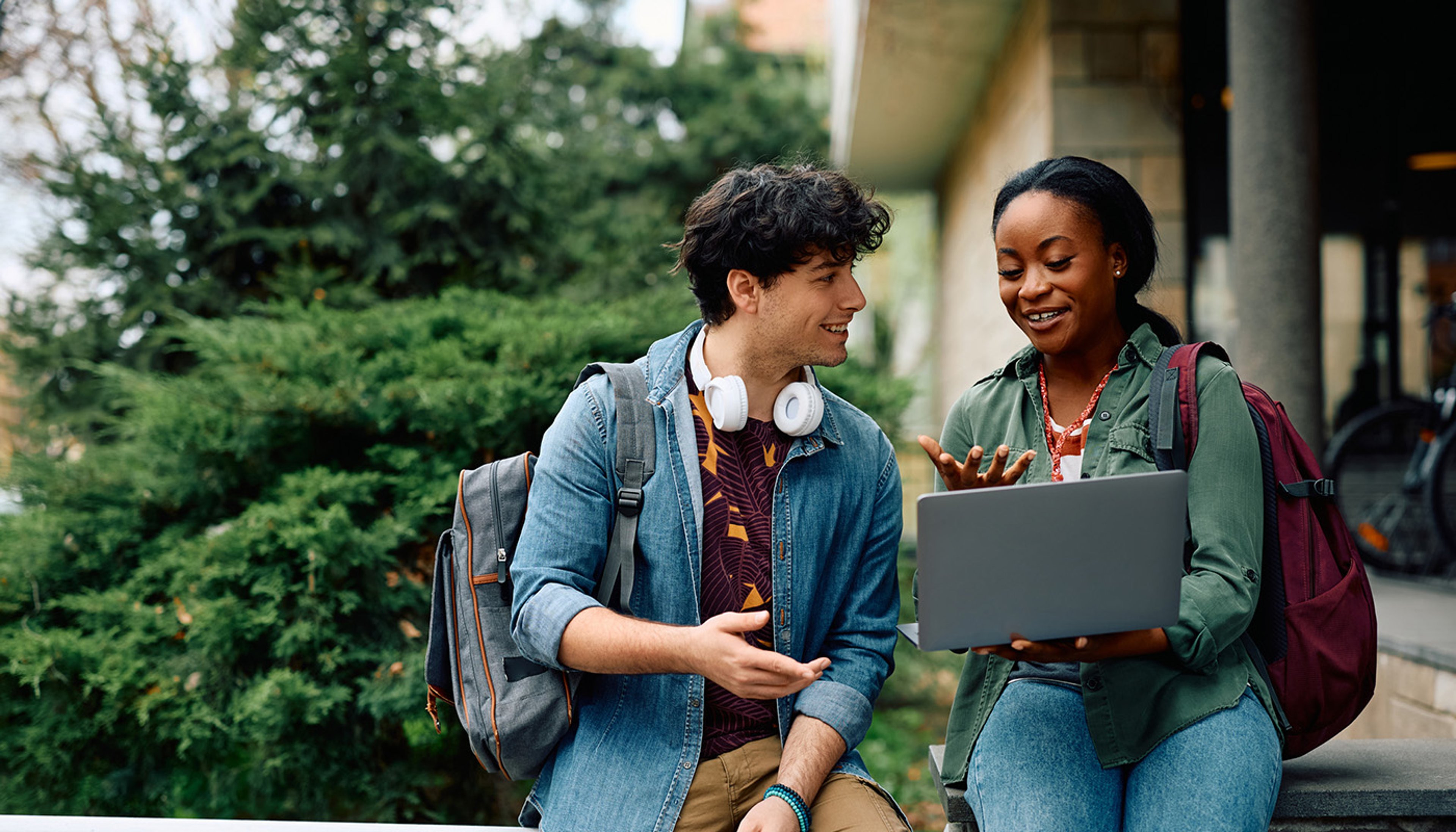 Two students on college campus smiling as they research information on laptop