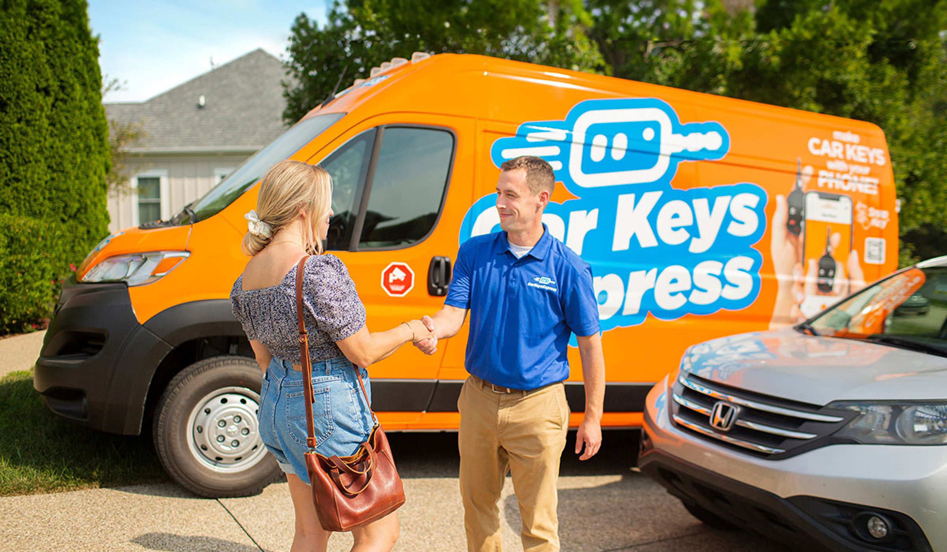 Car Keys Express technician in blue polo uniform handing car keys to woman in her driveway