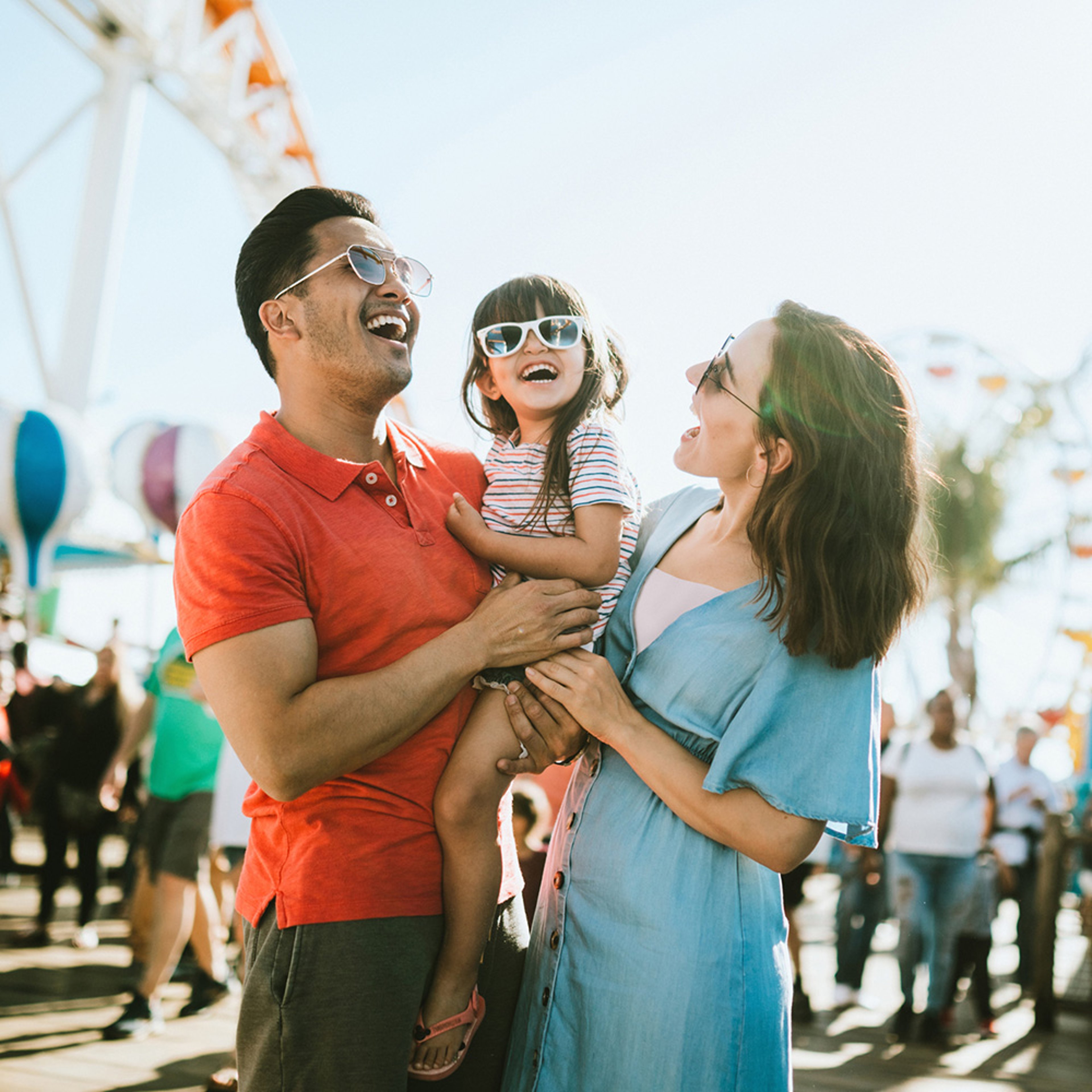Happy family of three wearing sunglasses at theme park with ferris wheel in the background