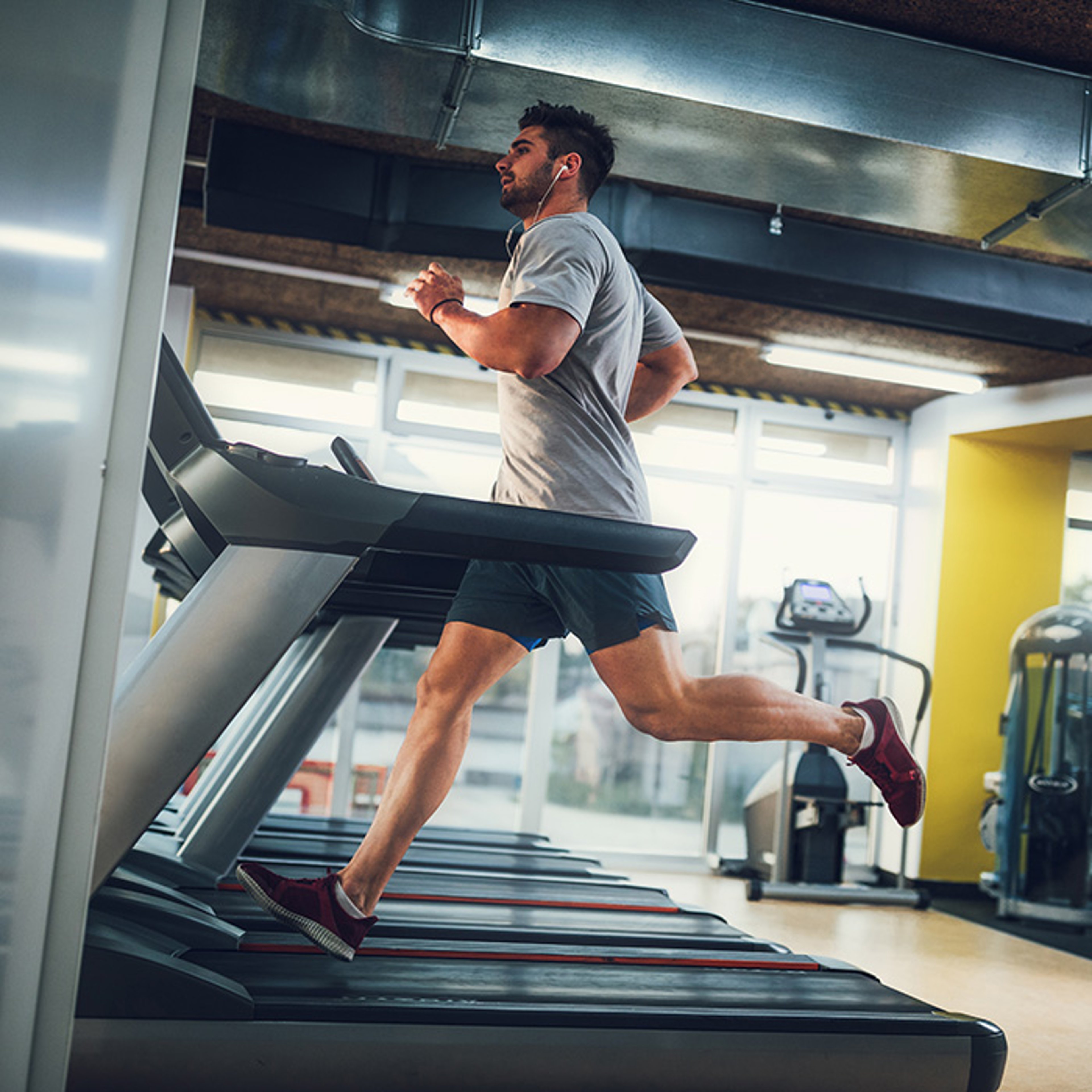 Middle-aged man in gray workout clothes exercising on treadmill in gym 