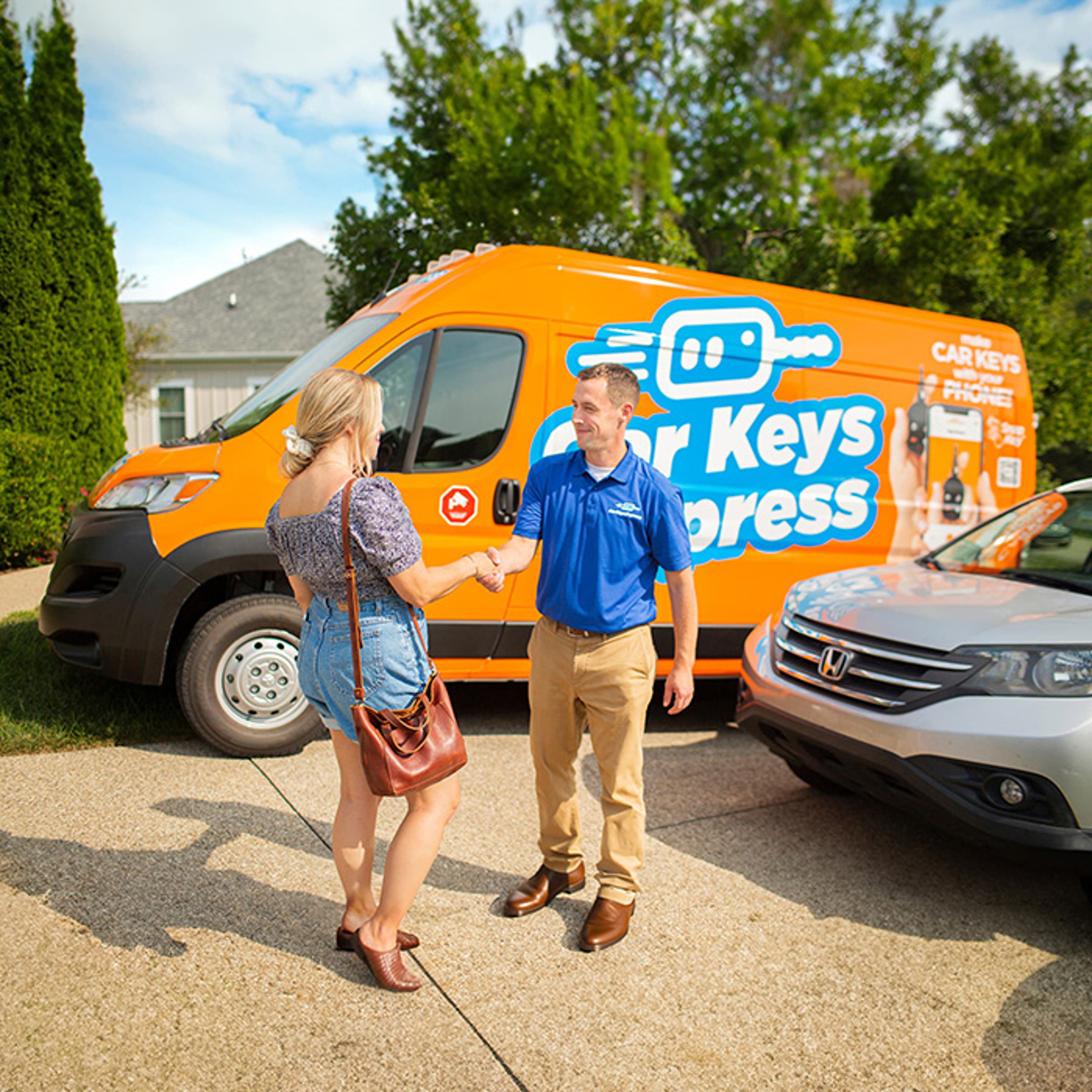 Car Keys Express service attendant standing in front of service van as he hands woman new key outside of her home
