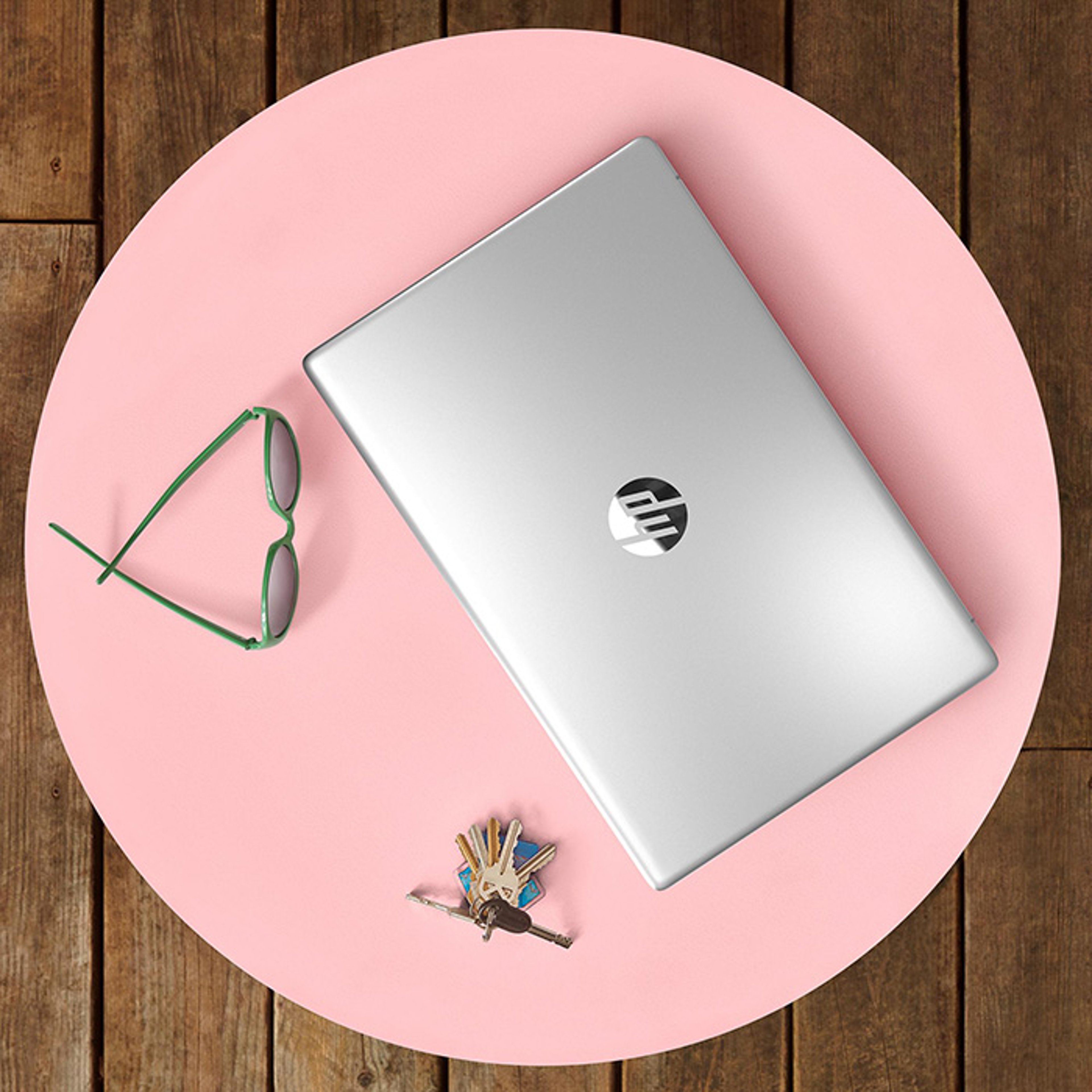 Silver HP laptop on top of pink circular mat with glasses