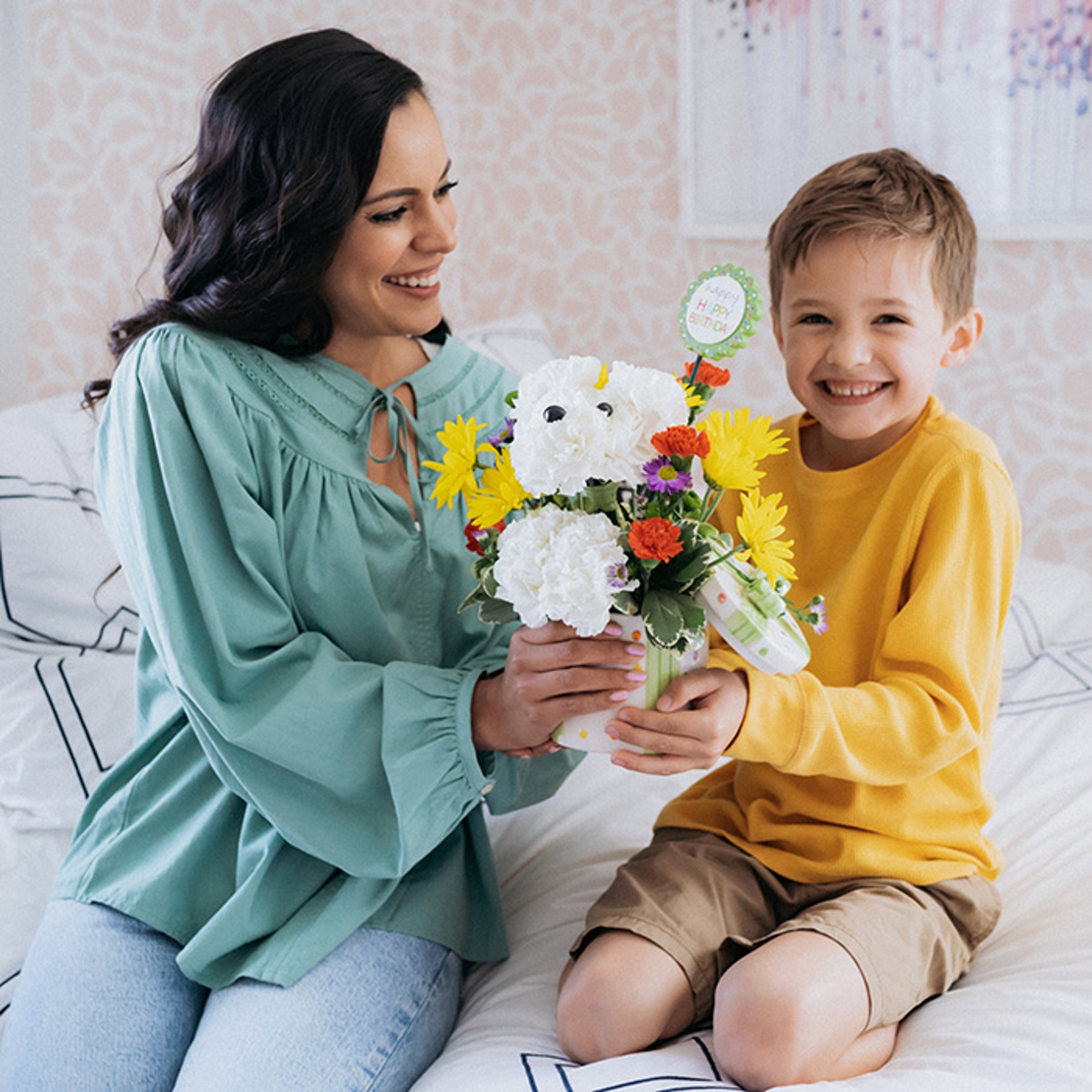 Happy mother and son holding white bear-shaped birthday floral arrangement