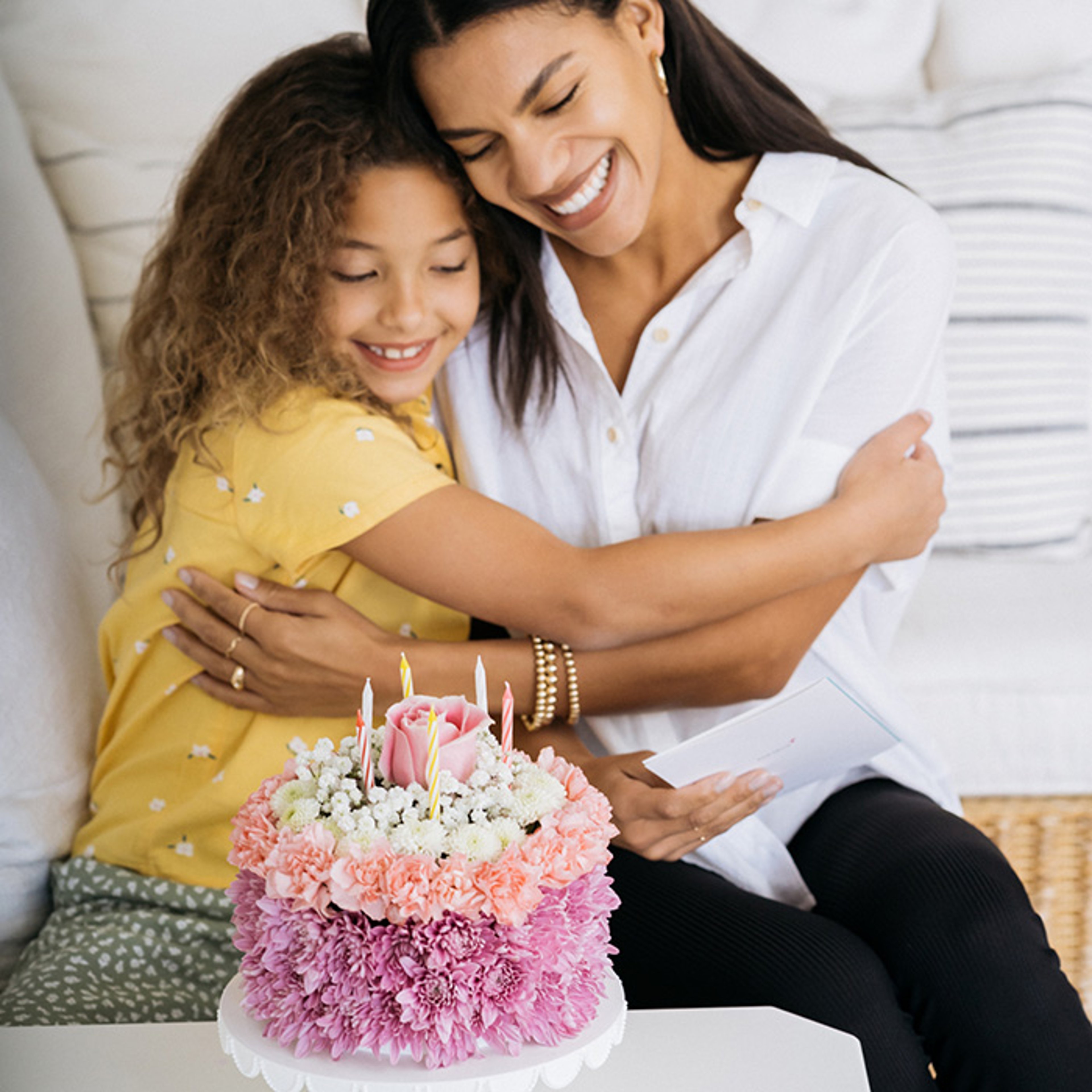 Mother and daughter embracing as they look down at pink birthday cake with candles