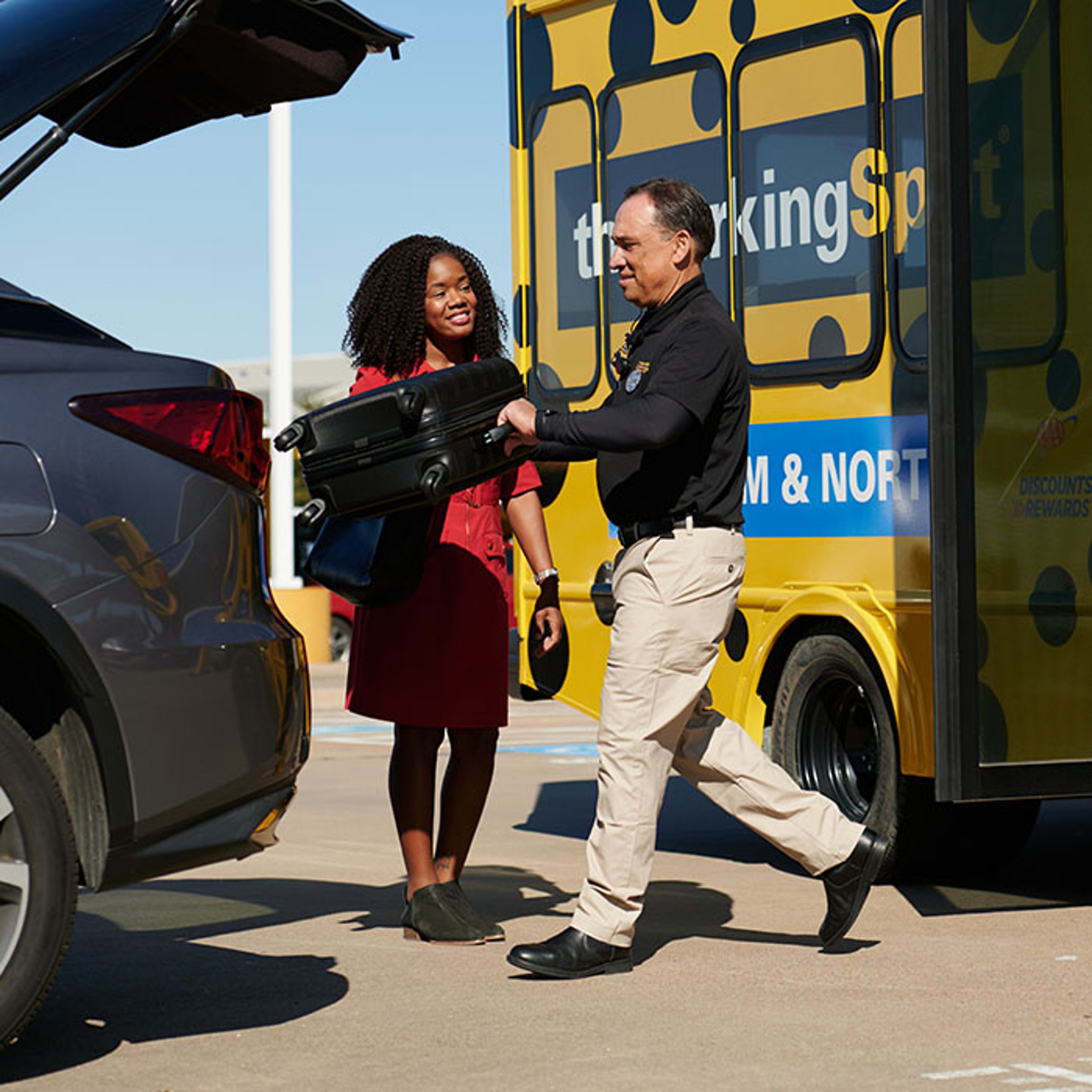 Business woman assisted by attendant as she boards The Parking Spot yellow and black bus