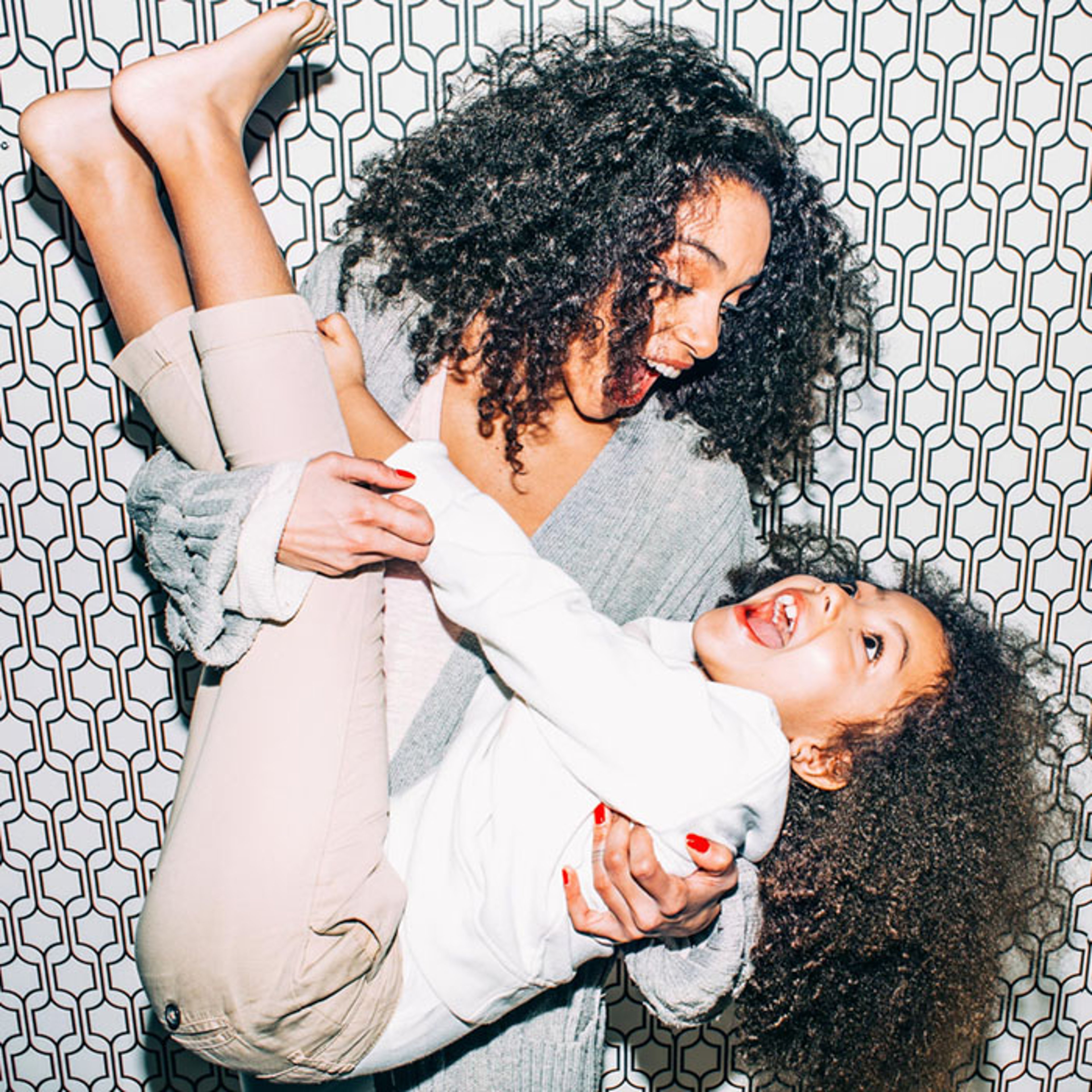 Mother playing with daughter and holding her upside down against photobooth backdrop