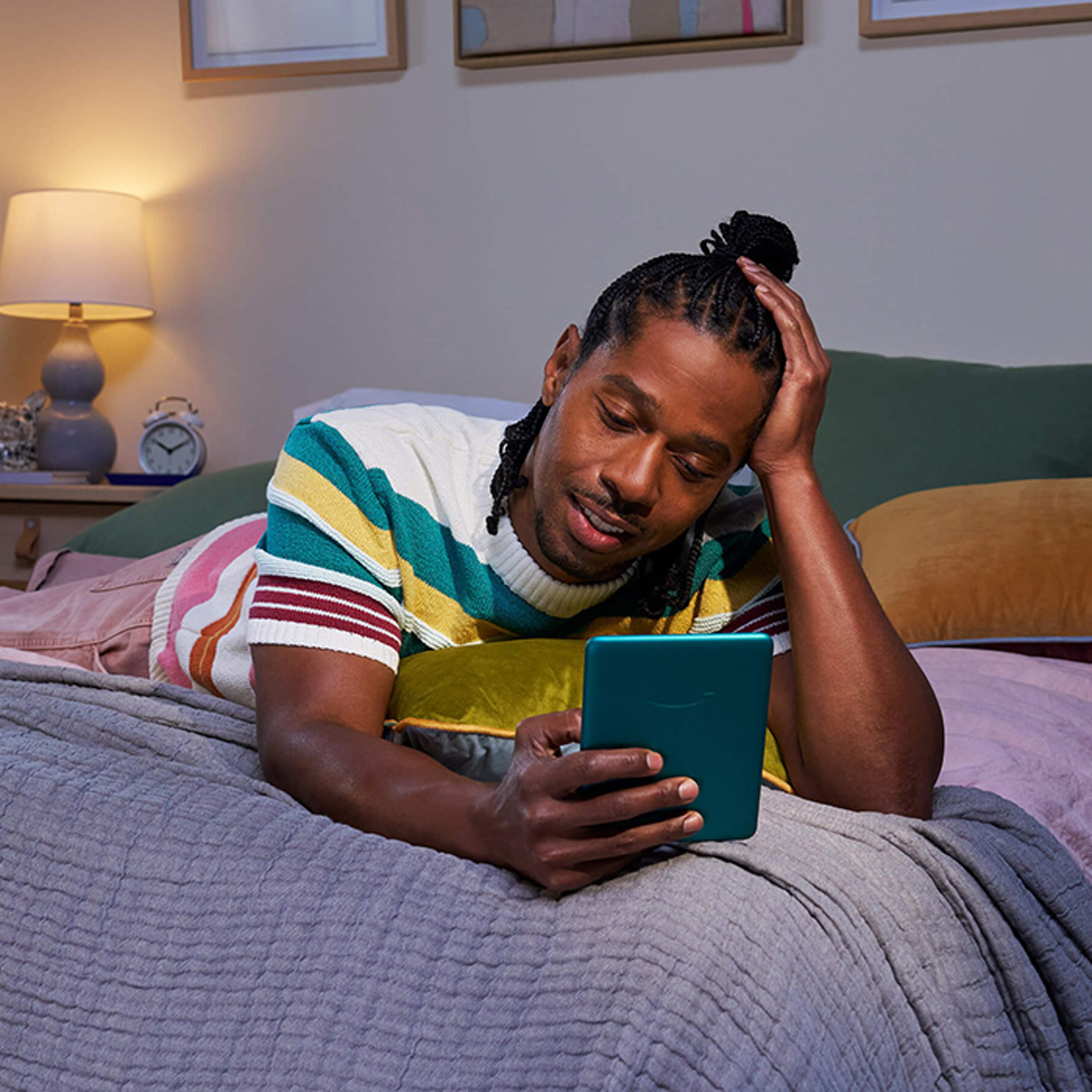 Young man laying on bed using small electronic tablet