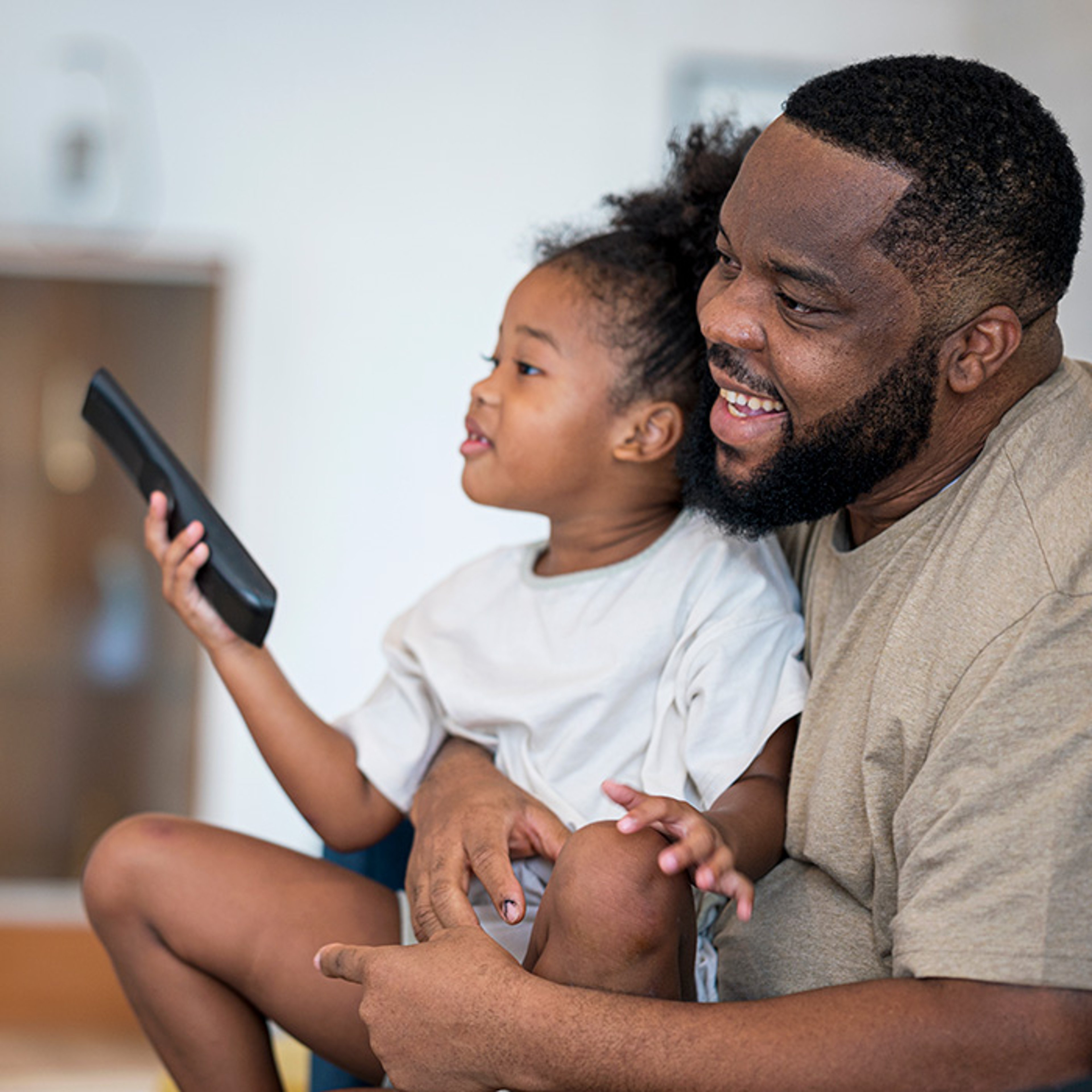 Father holding daughter as she holds remote tv control