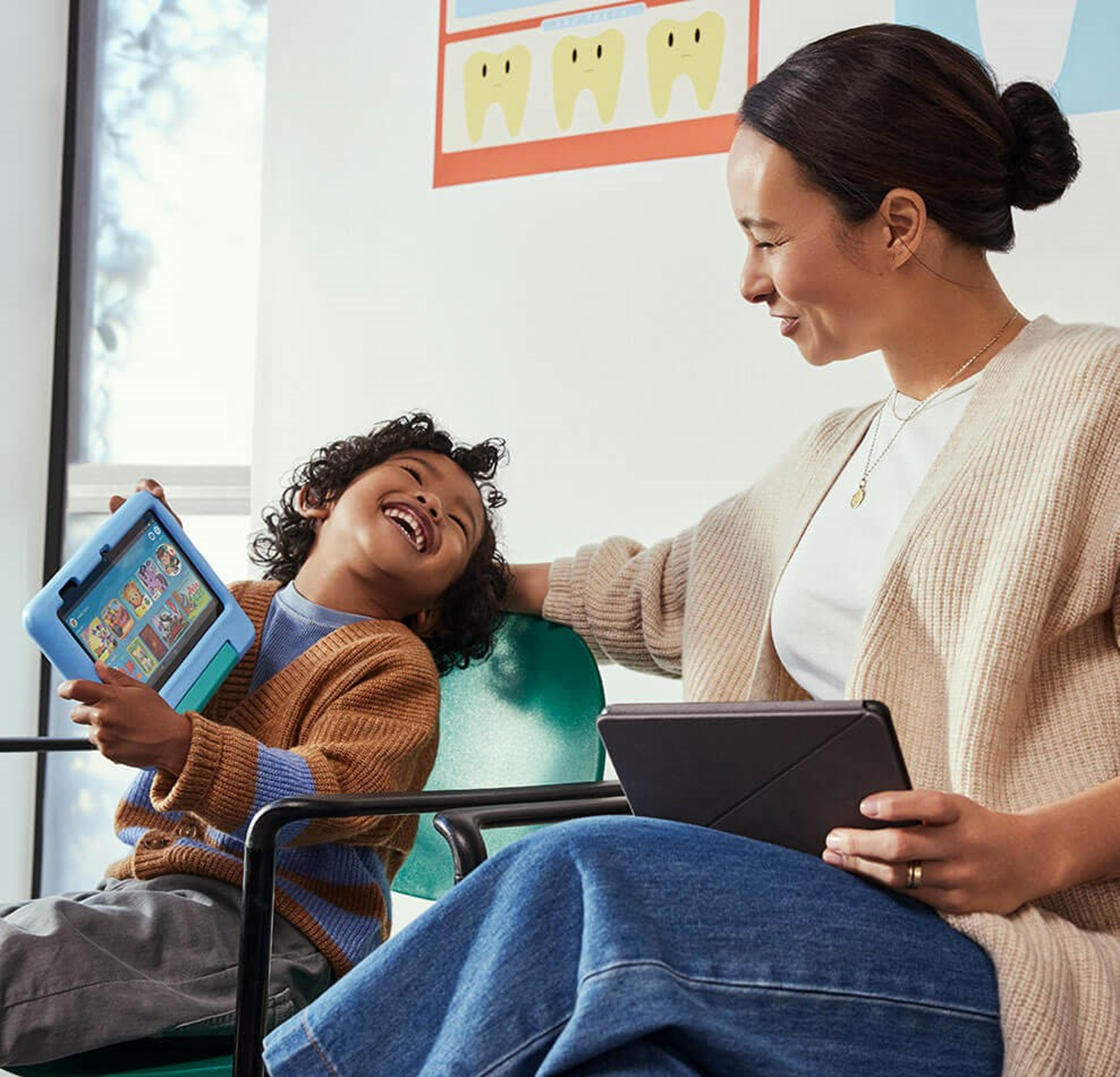 Mother and child smile while using tablets in a waiting room.