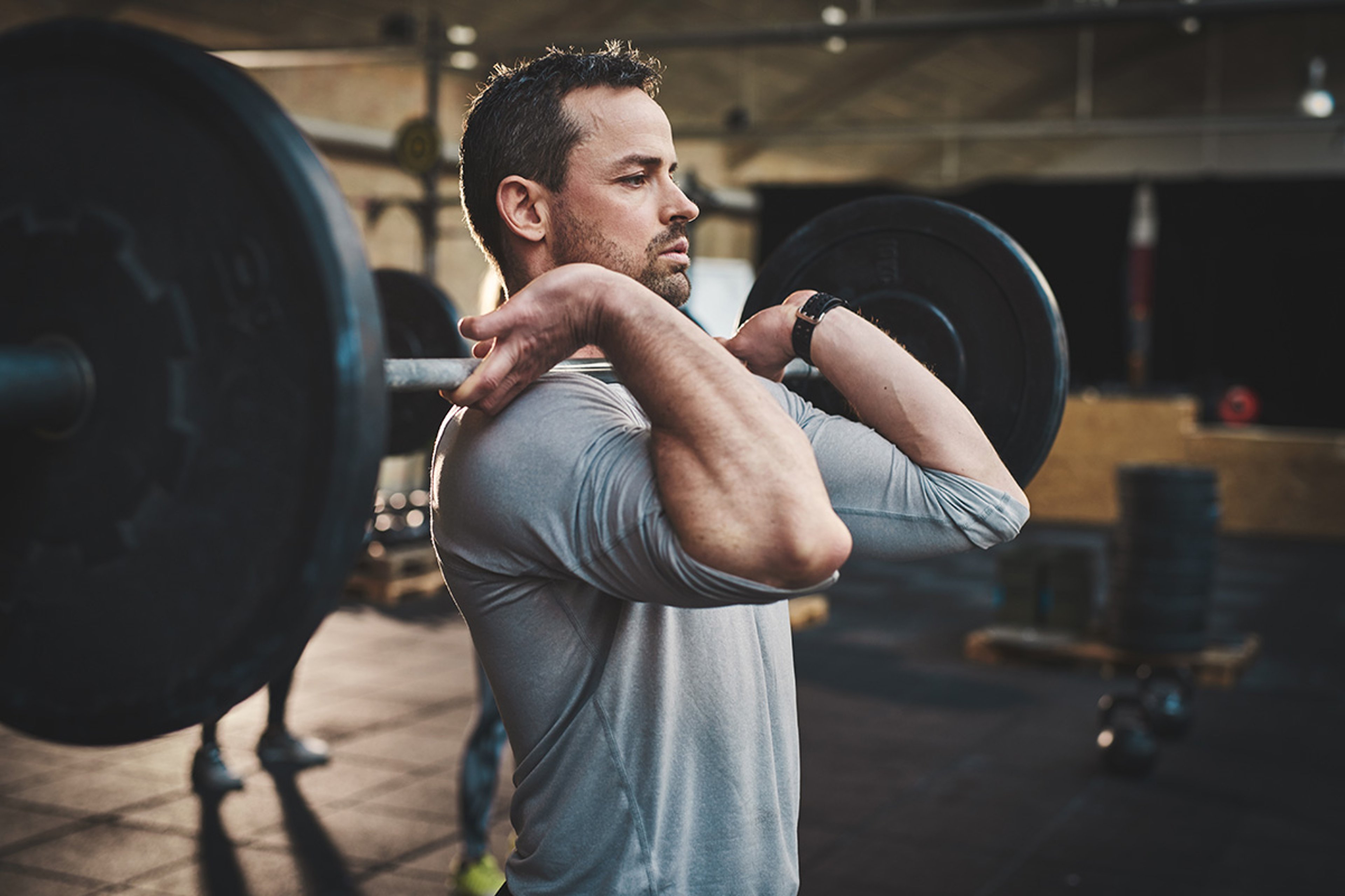 A man in a gym lifting a barbell in a front rack position.