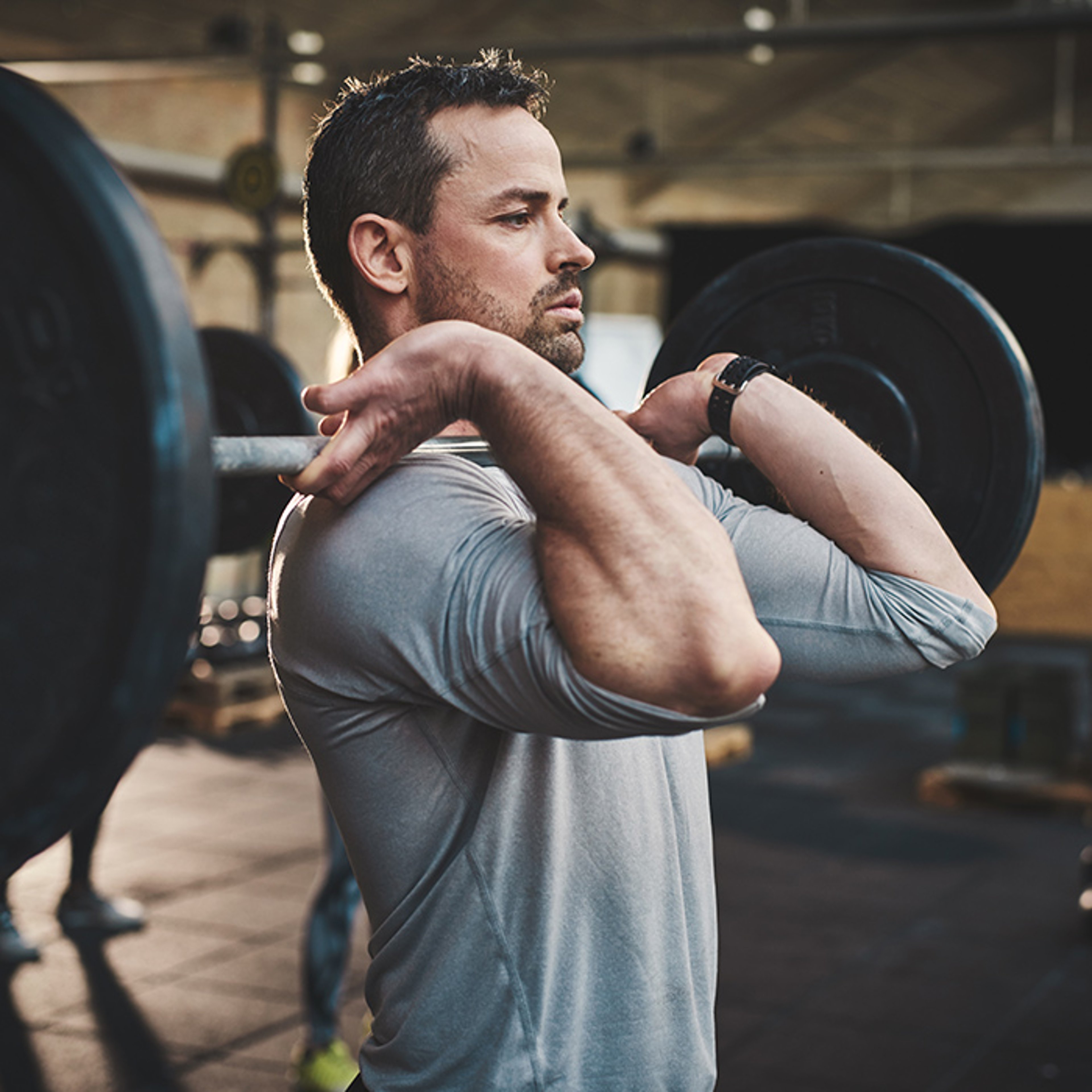 Man performing a front squat with a barbell in a gym.