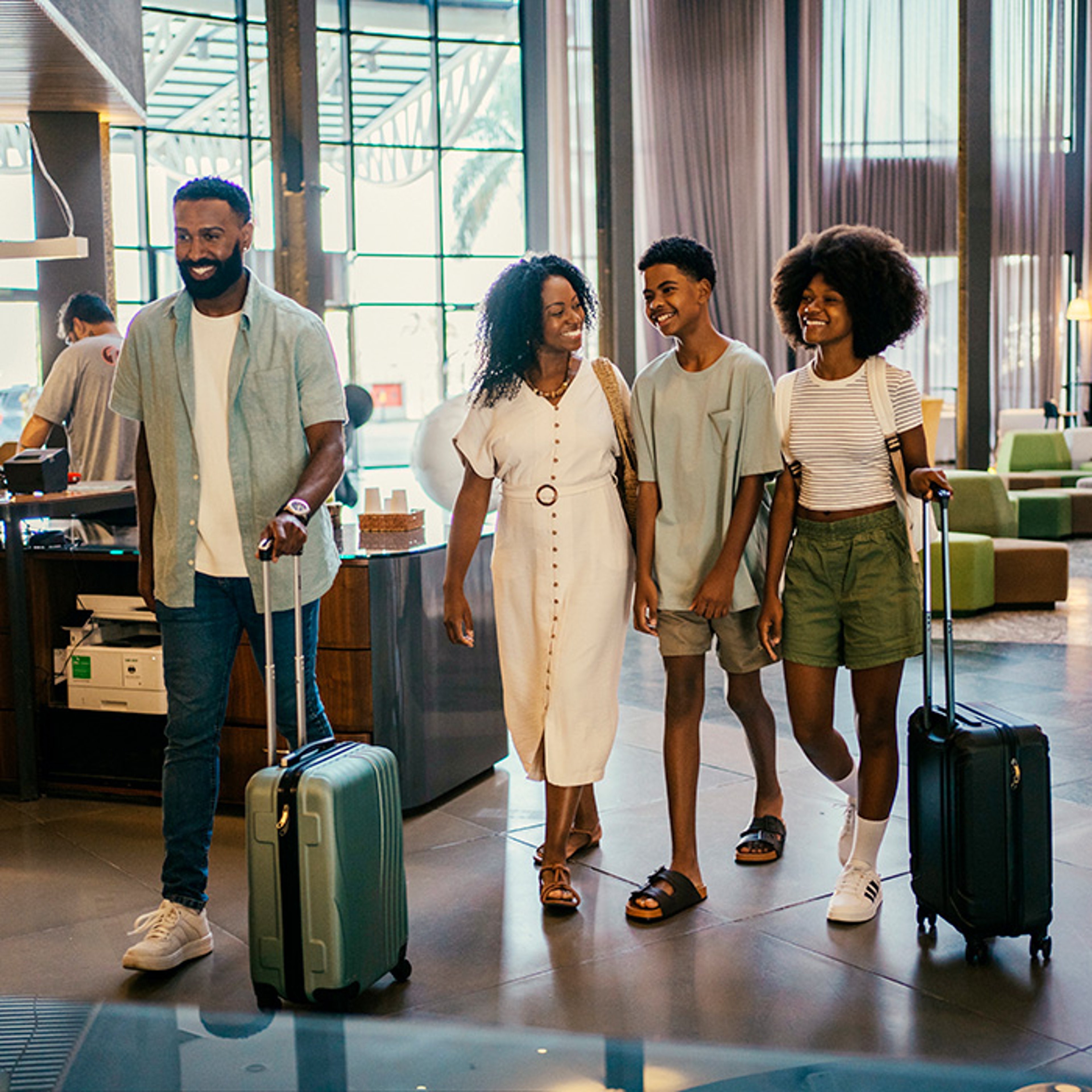 A family of four with luggage walking through a hotel lobby.