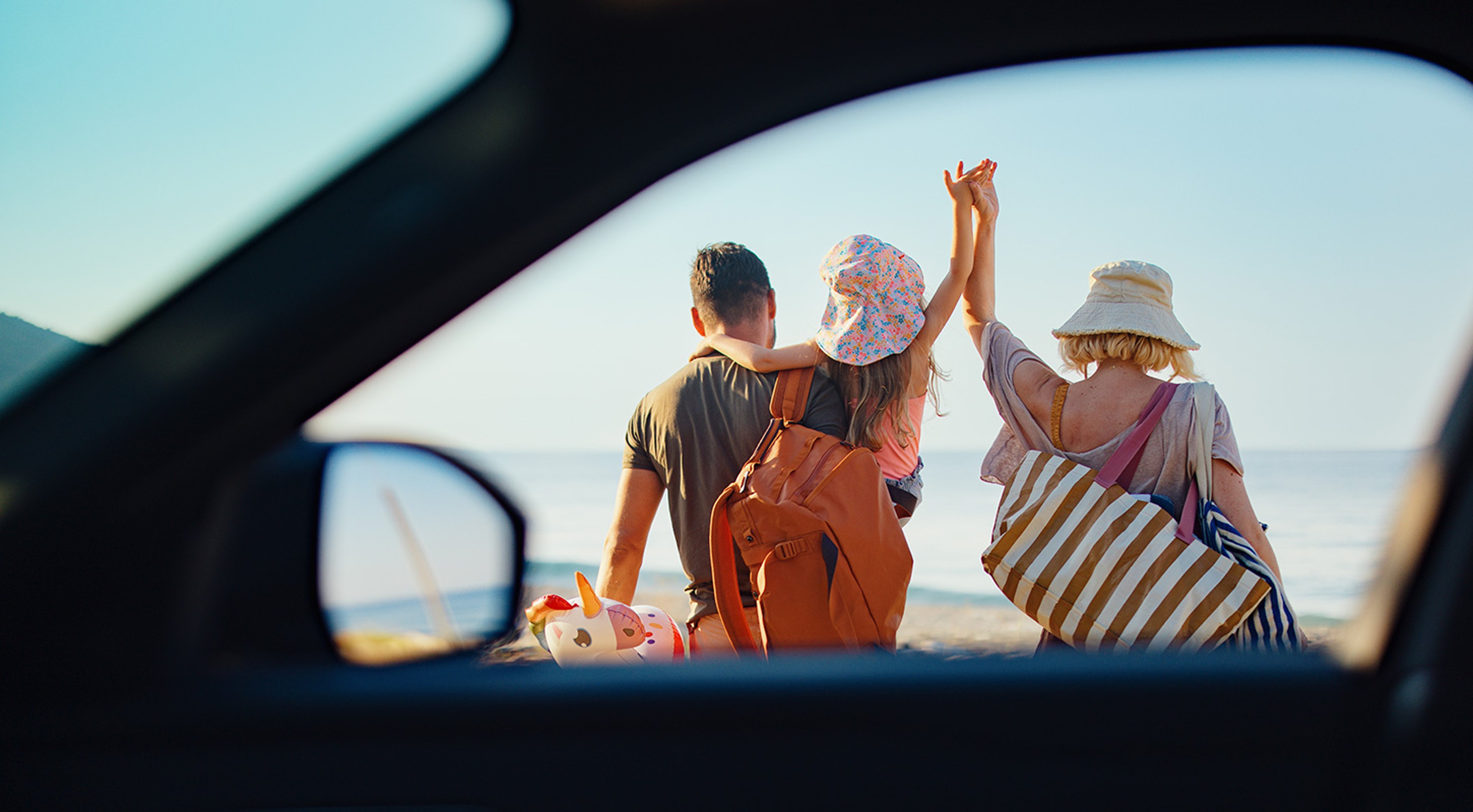 Family walking towards a beach, seen through a car window.