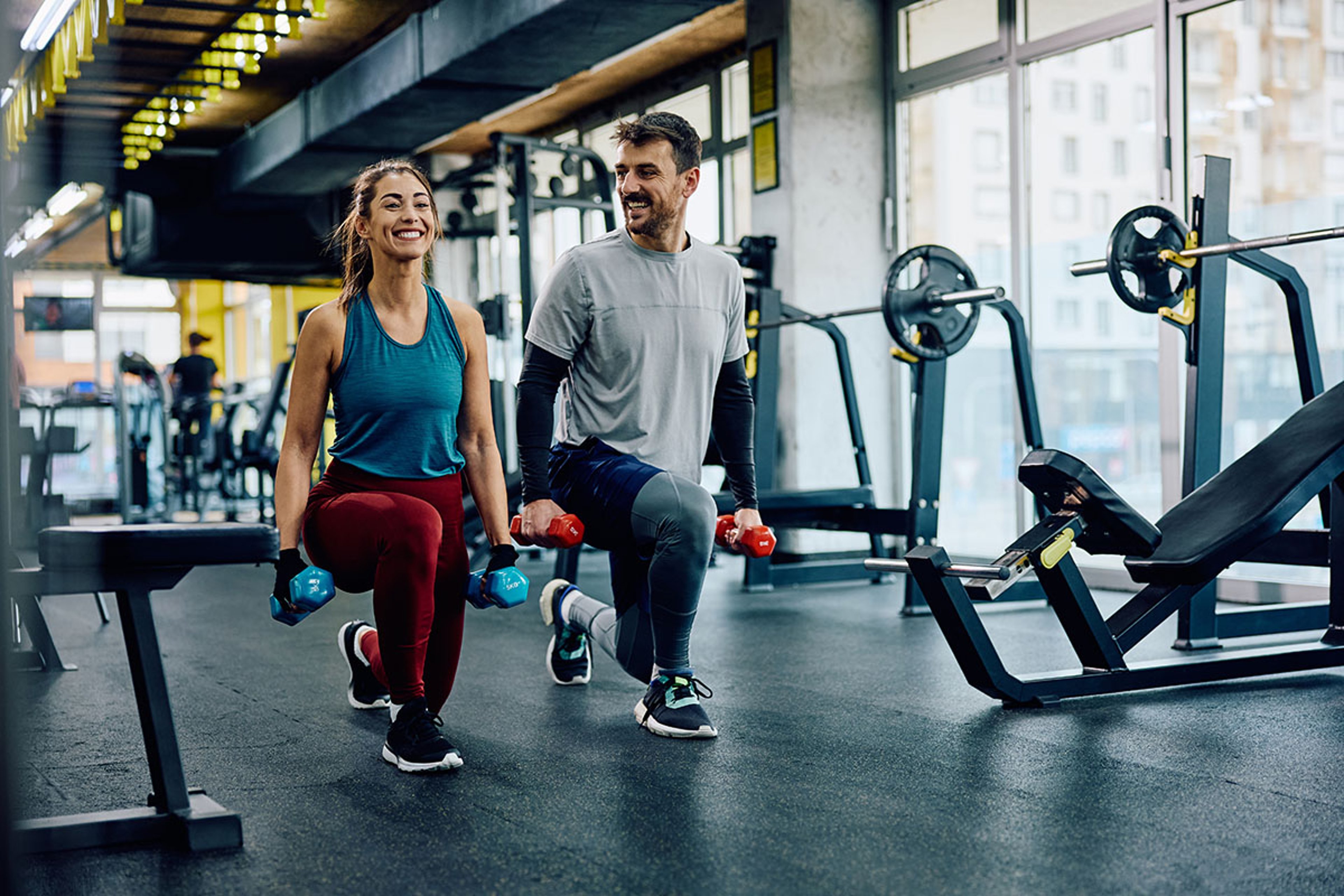 Couple doing lunges with dumbbells in gym