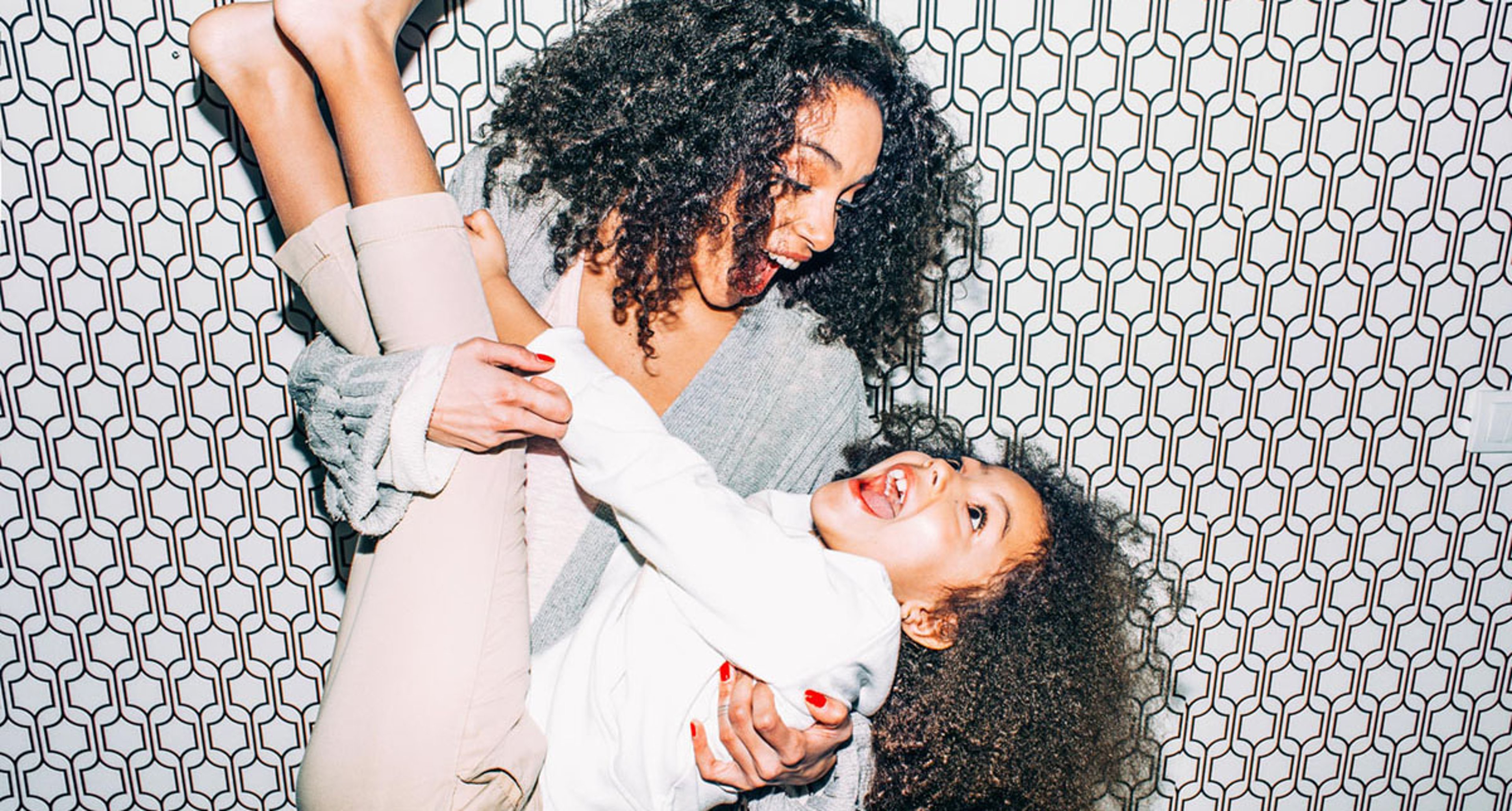 Happy mother and daughter with curly hair playing together in front of a patterned wall.