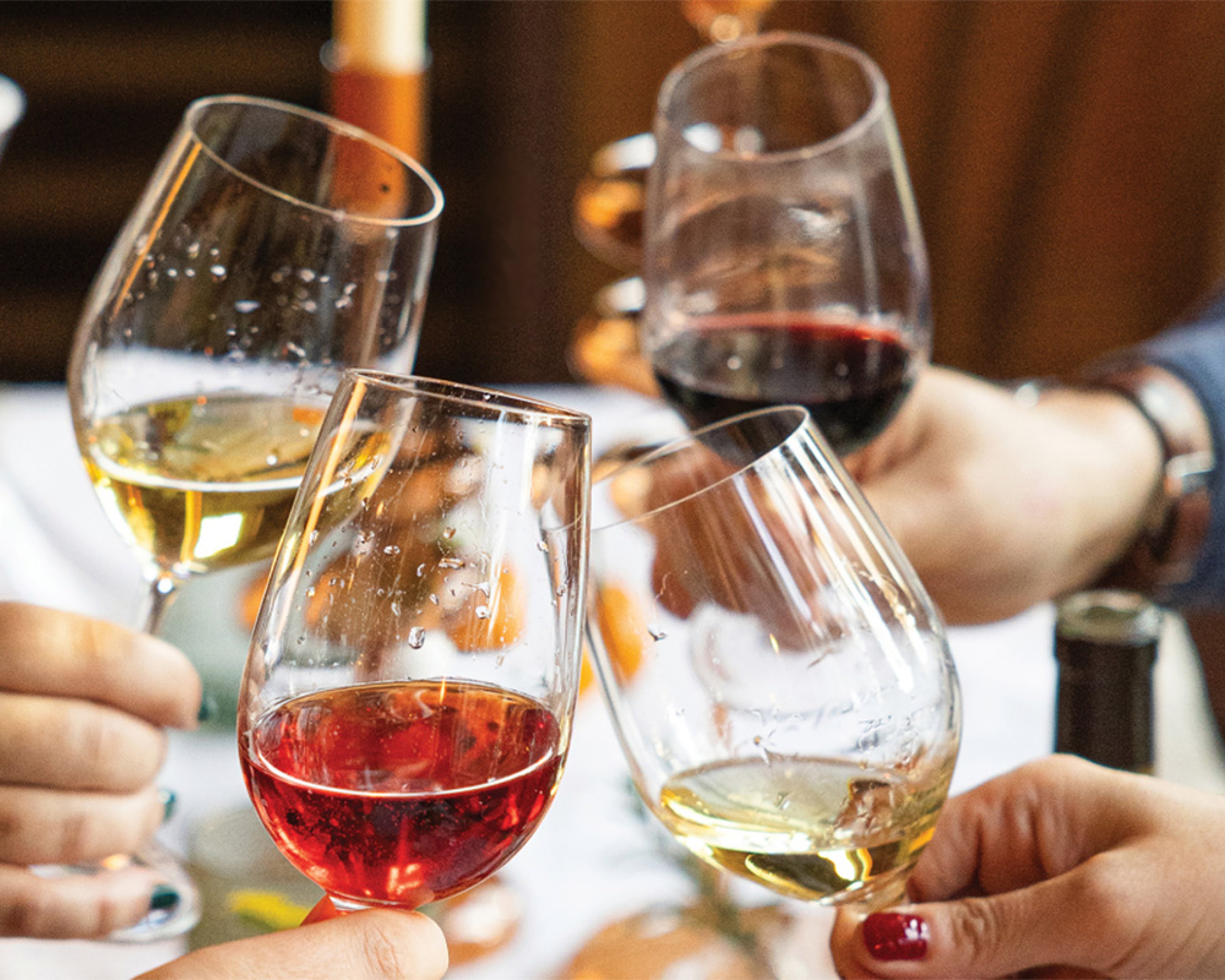 Close up of hands of four friends toasting wine glasses at upscale dinner