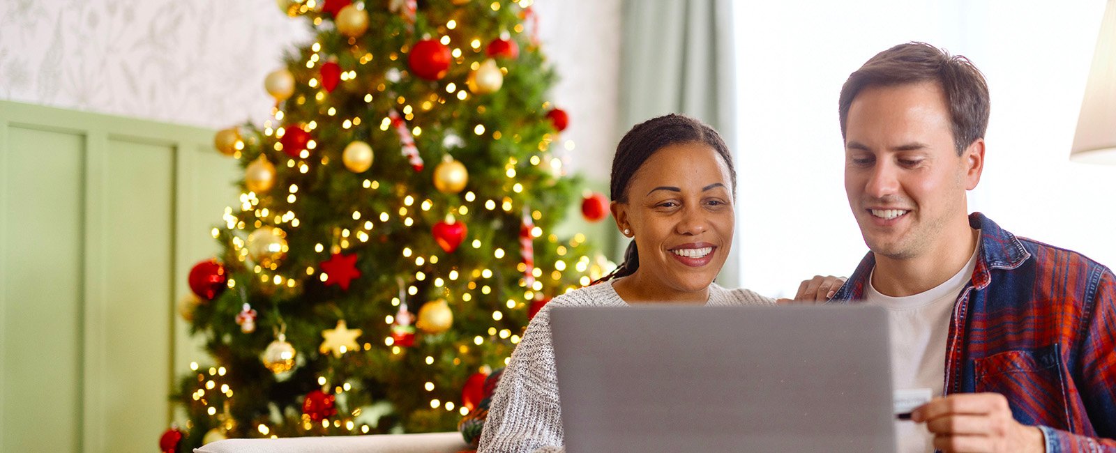 Happy couple browsing on laptop with Christmas tree in background