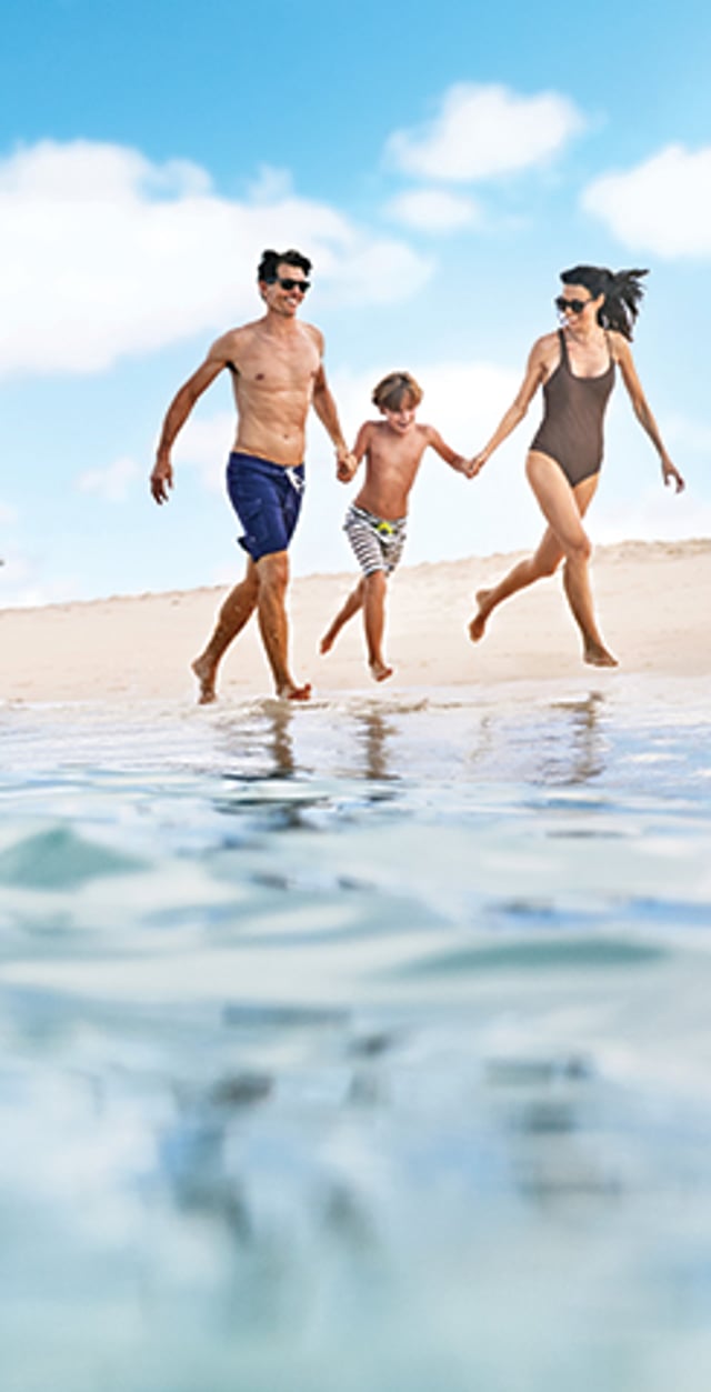 Family of three holding hands and running along the shoreline.