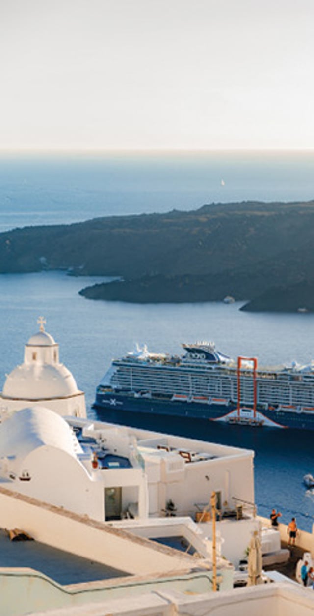Celebrity cruise ship sailing past the whitewashed buildings of Santorini, Greece.