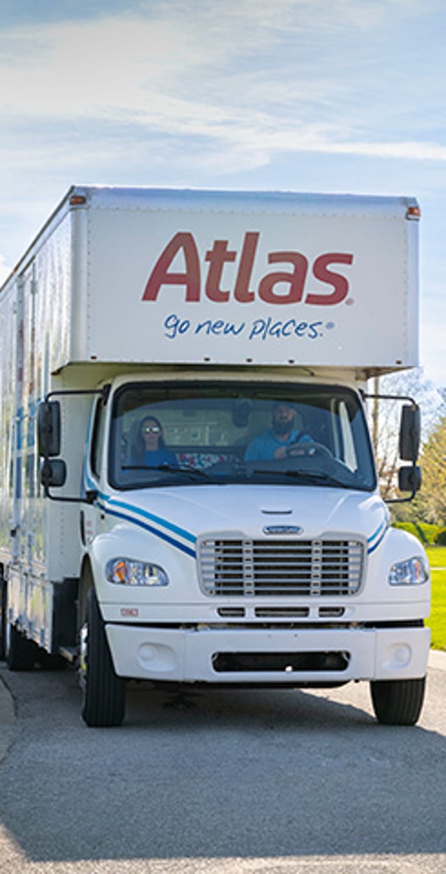 Atlas moving truck parked outdoors with two people visible through the windshield.