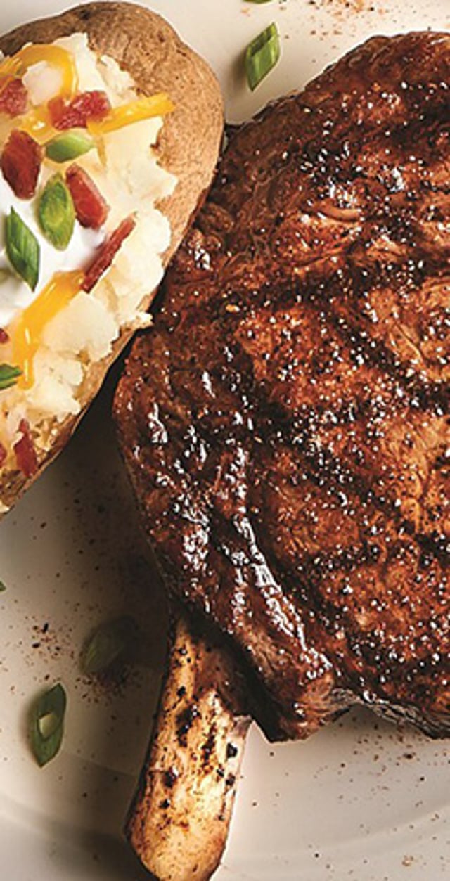 Grilled steak served with a loaded baked potato topped with cheese, bacon, and green onion.