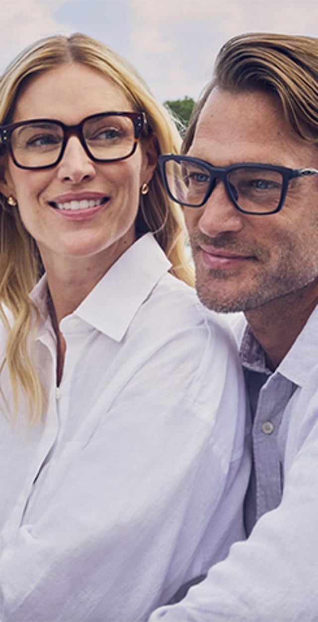 Two adults wearing eyeglasses sitting outdoors and looking off into the distance.